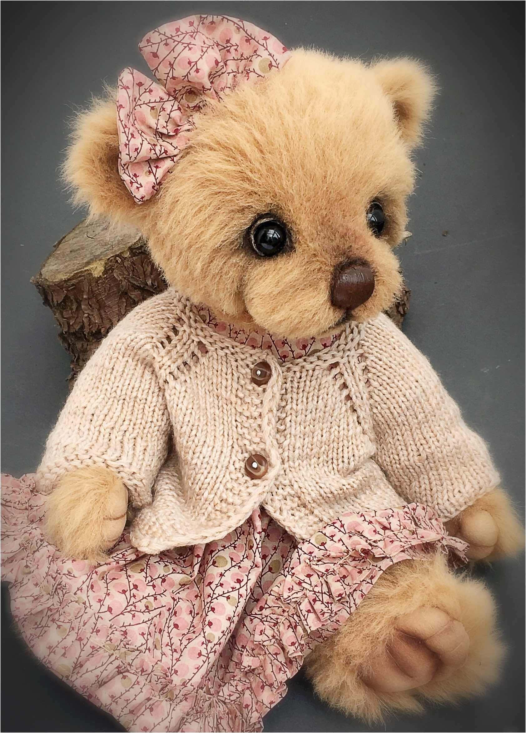 Cute Teddy 桌布 壁紙 — 一隻柔軟的米色泰迪熊穿著粉紅色花卉連衣裙和針織開衫，輕輕坐在深灰色背景的樹樁上。