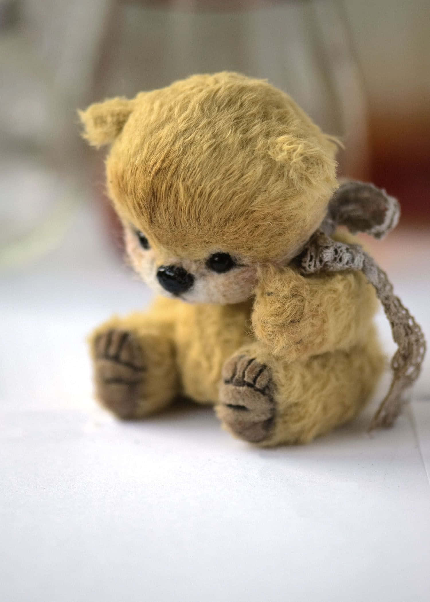 Cute Teddy 桌布 壁紙 — 一隻柔軟的金色泰迪熊，帶有紋理絨毛，靜靜地坐在白色表面上，脖子上圍著一條鉤織圍巾。