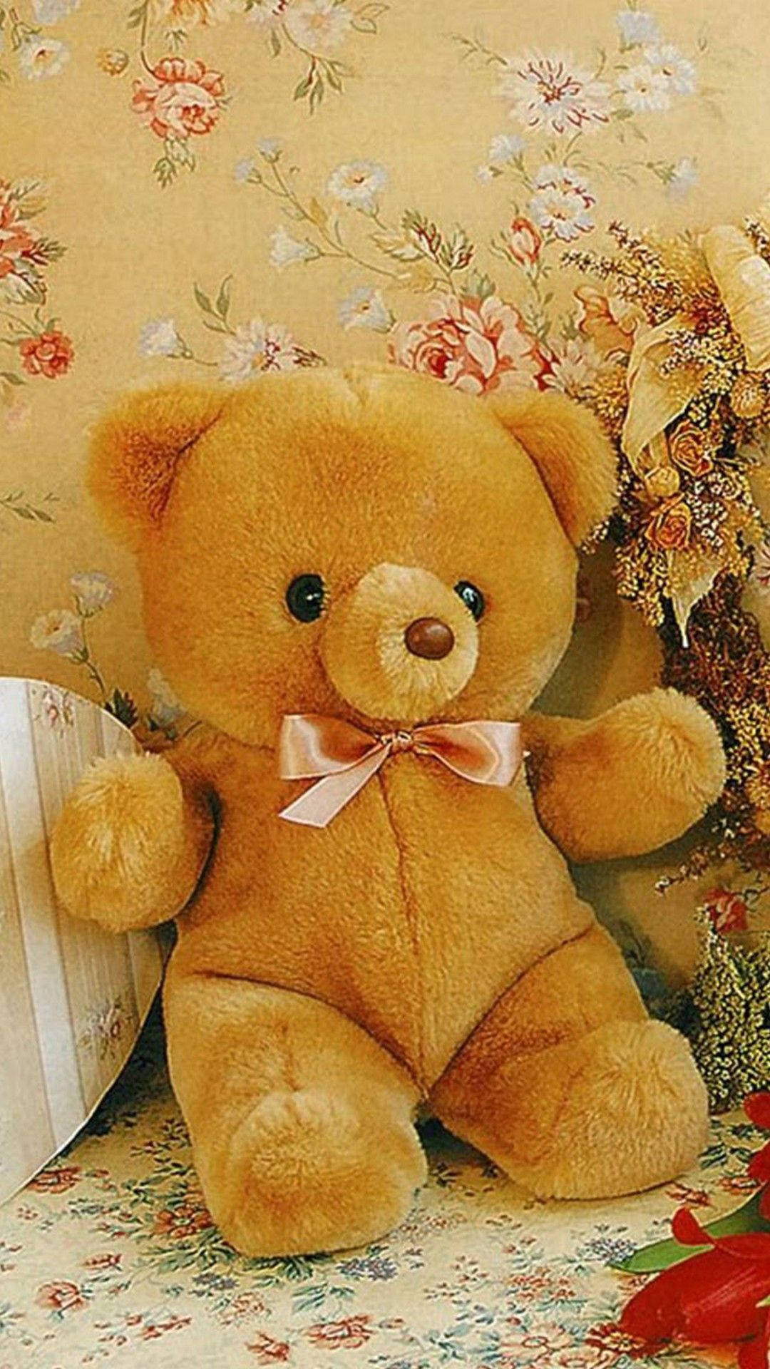 Teddy Bear 桌布 壁紙 — 一隻柔軟的金色泰迪熊繫著粉紅色蝴蝶結，坐在花卉壁紙上，旁邊有一個裝飾花束。