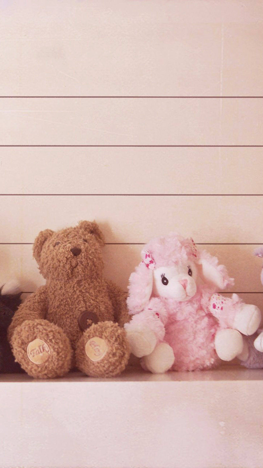 Cute Bear 桌布 壁紙 — 一隻棕色泰迪熊和粉紅色毛絨小羊布偶並排坐在淺色木紋牆前的木架上。