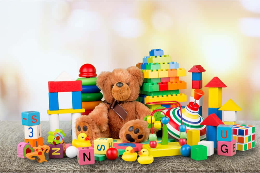 toys 桌布 壁紙 — 一隻棕色泰迪熊坐在有紋理的表面上，周圍環繞著色彩繽紛的積木、字母、橡膠鴨子和玩具。