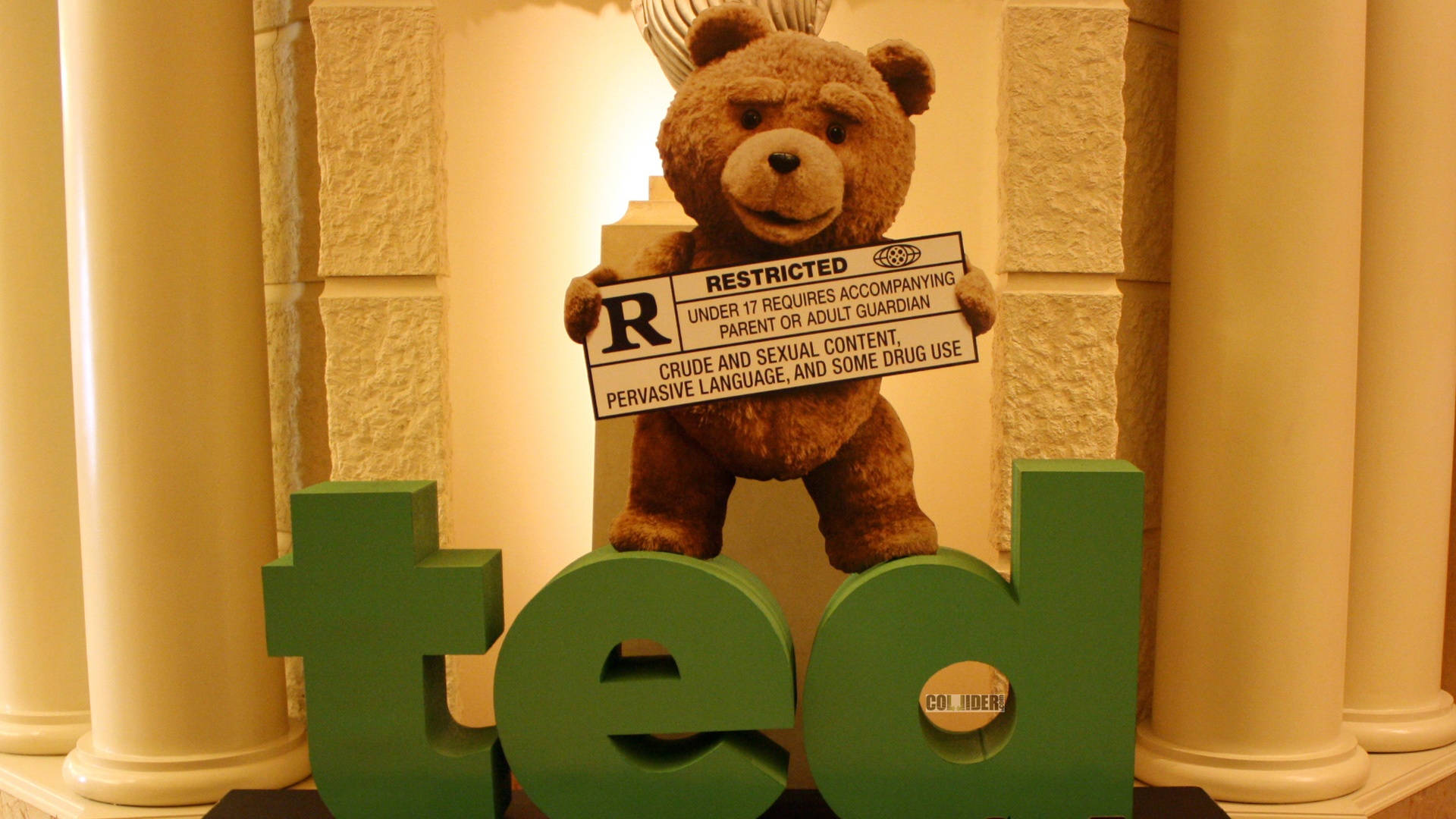 Ted 桌布 壁紙 — 一隻棕色泰迪熊拿著限制級電影評級標誌，站在溫暖照明的石柱環境中，背後是巨大的綠色「ted」字母。