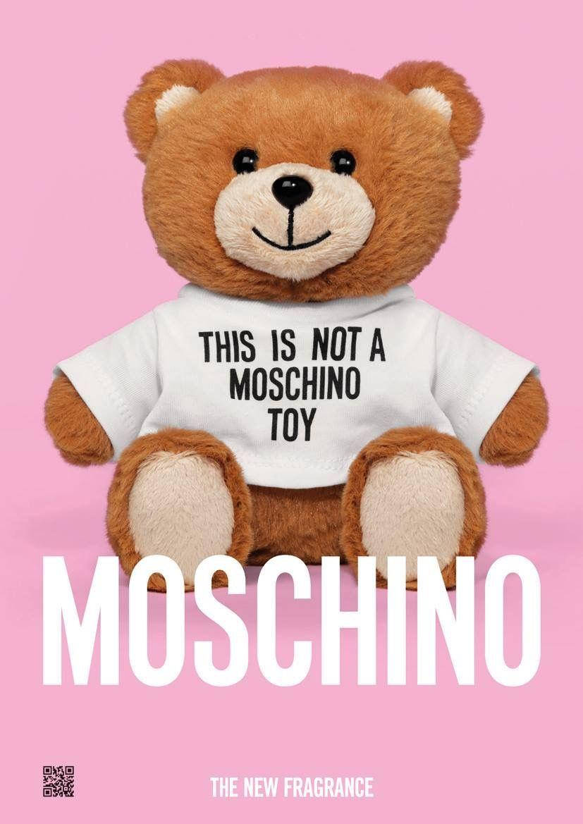 moschino 桌布 壁紙 — 一隻棕色泰迪熊穿著白色T恤，上面有文字，坐在純粉紅色背景前，帶有大型白色品牌標誌。