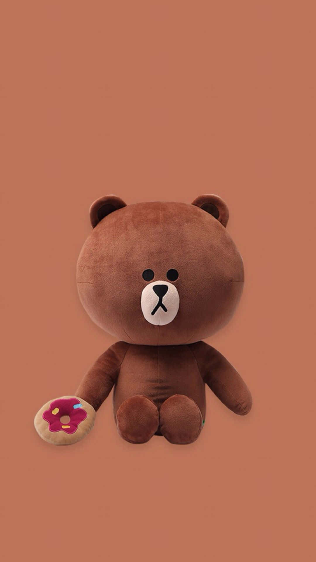 Teddy Bear 桌布 壁紙 — 一隻棕色絨毛熊，白色口鼻，在純色赤陶背景前拿著一個粉紅色糖霜甜甜圈。