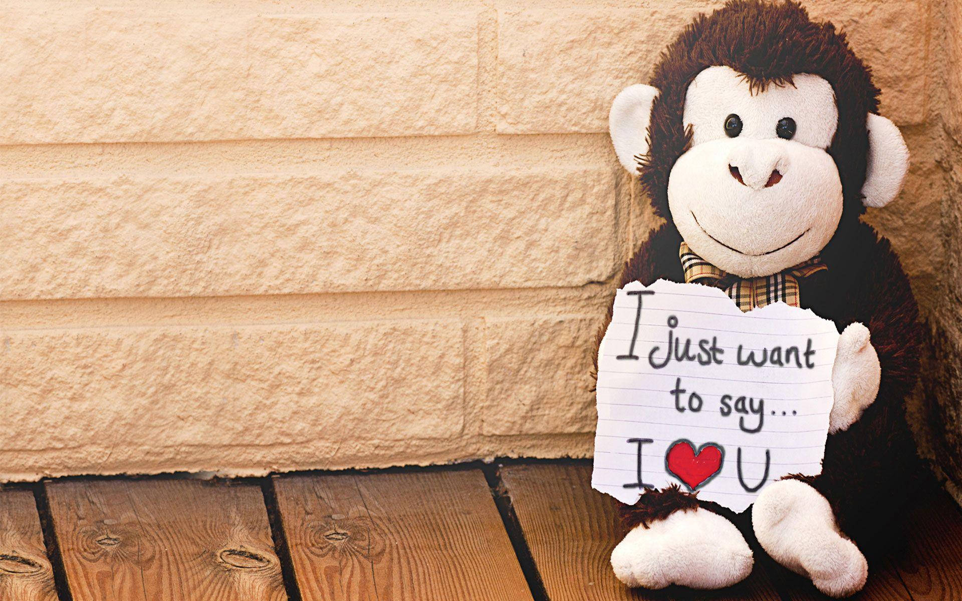 Monkey 桌布 壁紙 — 一隻棕色絨毛猴子手持一張手寫便條，上面寫著『I just want to say... I ❤️ U』，背景是石牆和木地板。