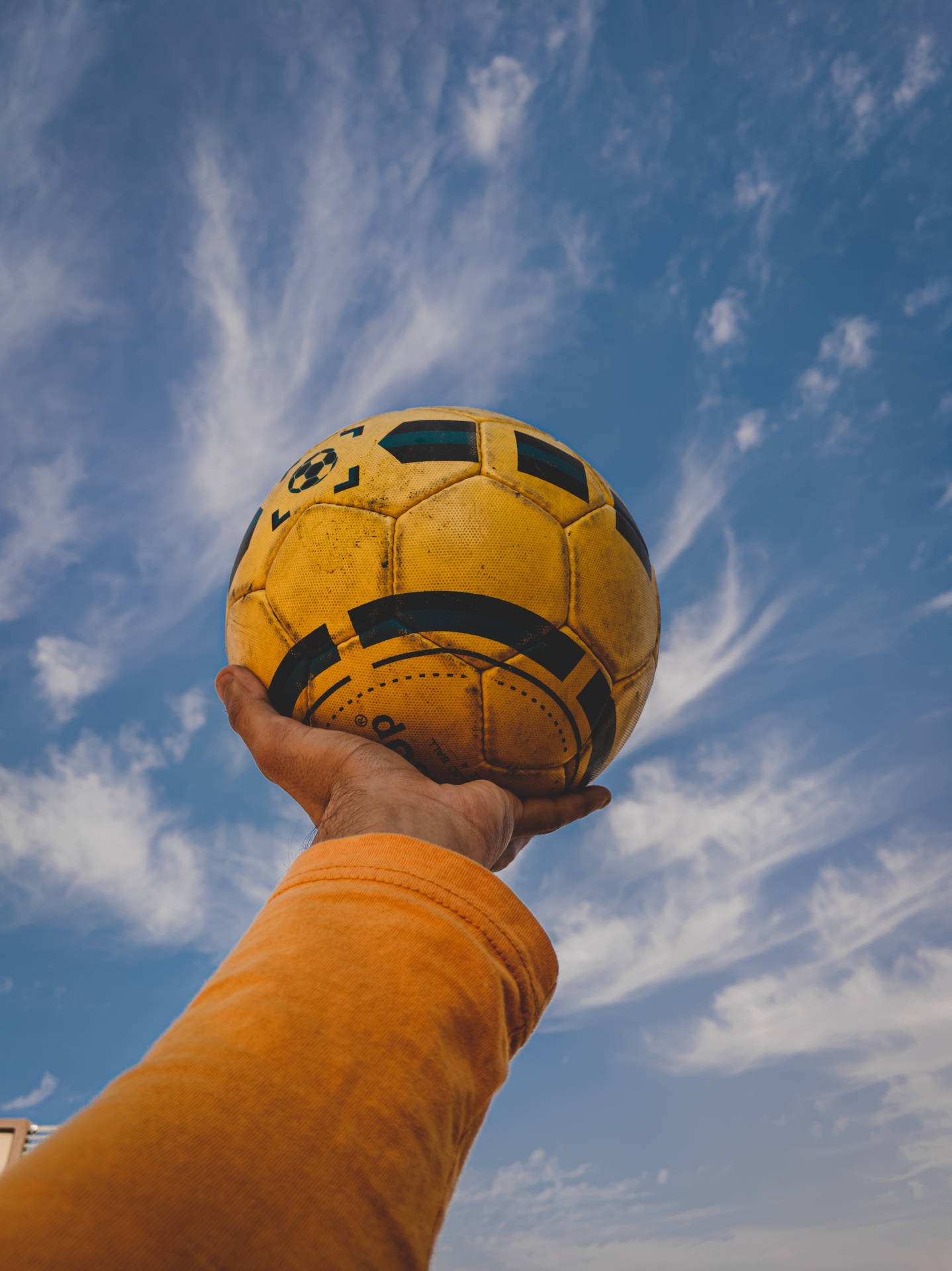 手在藍天白雲下拿著黃色足球 — Google pixel 壁紙