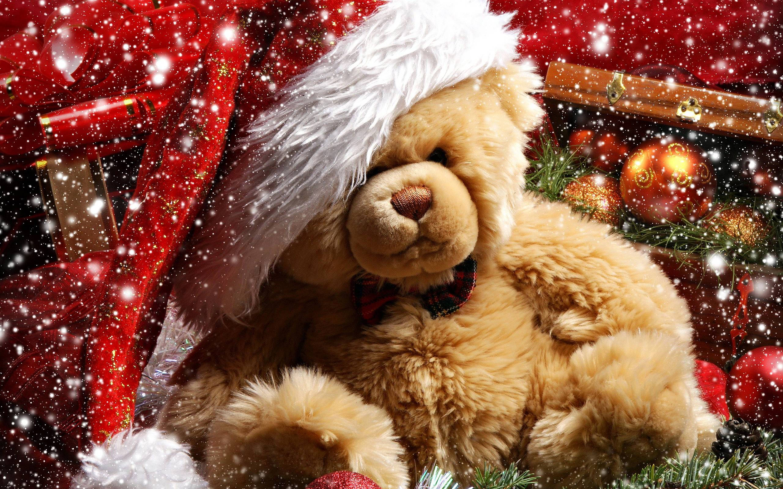 Teddy Bear 桌布 壁紙 — 一隻毛茸茸的棕色泰迪熊戴著聖誕帽和蝴蝶結，坐在飄落的雪花和節日紅色裝飾品中。