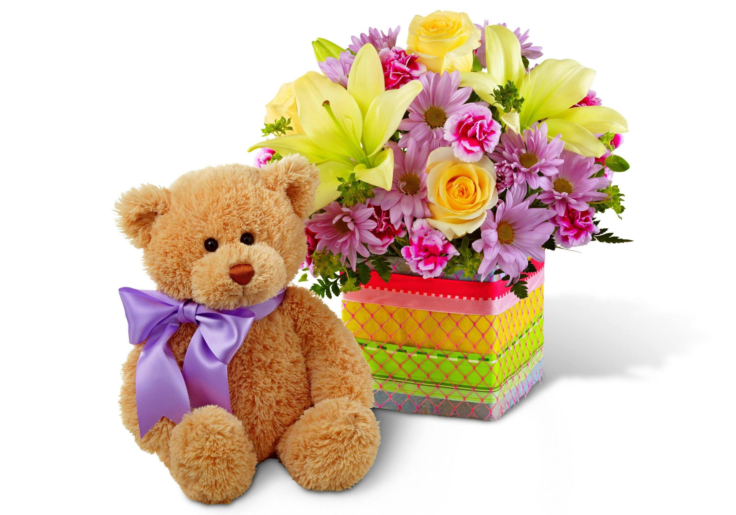 Happy Birthday Flower 桌布 壁紙 — 一隻毛茸茸的棕色泰迪熊繫著紫色蝴蝶結，坐在一個色彩繽紛圖案盒子裡，旁邊是充滿活力的花卉佈置。