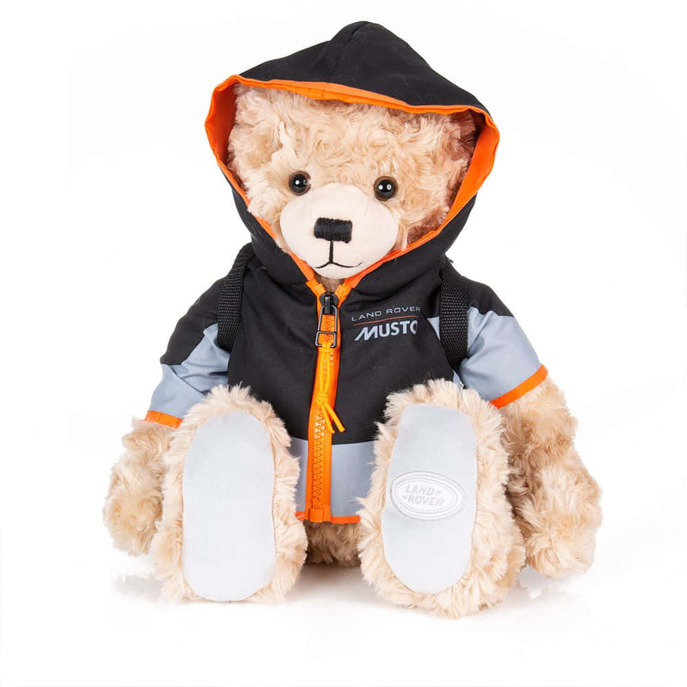 Teddy Bear 桌布 壁紙 — 一隻毛茸茸的淺棕色泰迪熊，穿著黑色和橙色的 Land Rover Musto 外套，帶有灰色點綴和品牌鞋底，坐在白色背景前。