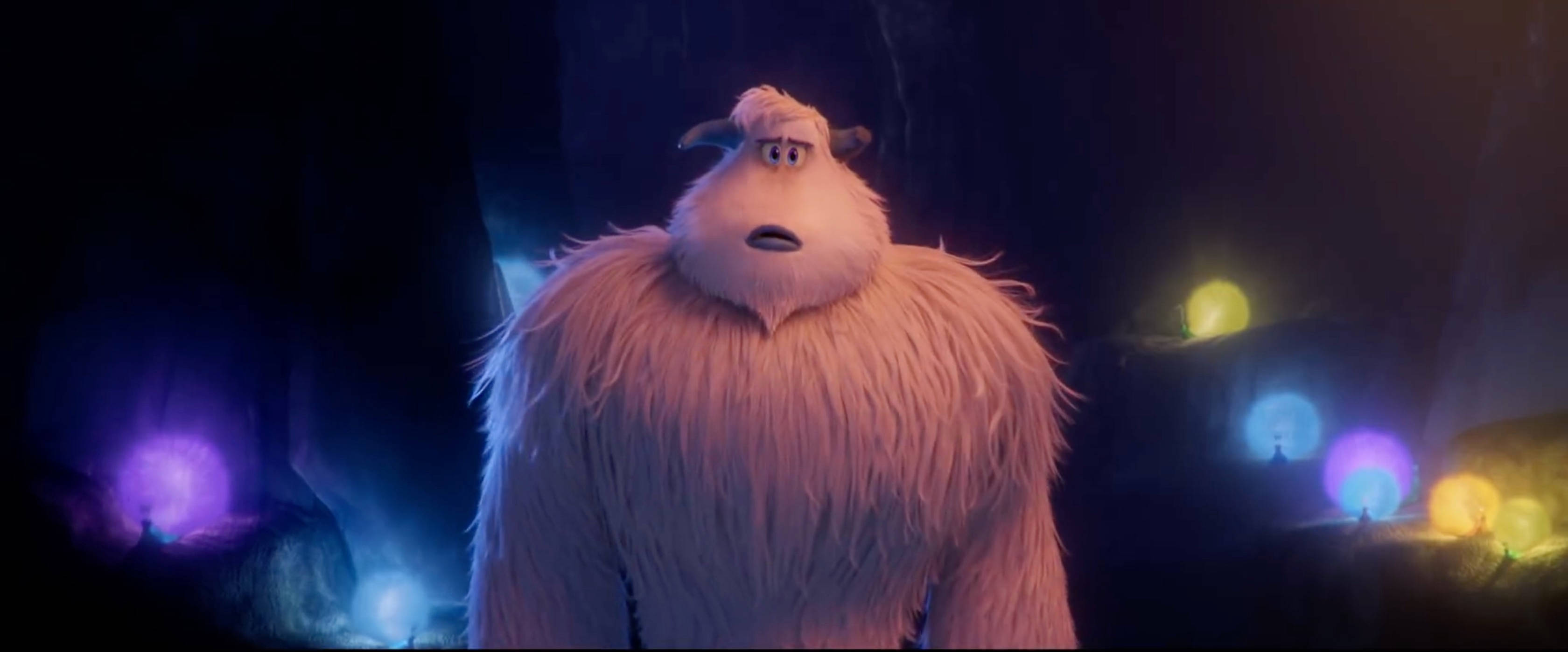 Smallfoot 桌布 壁紙 — 一隻毛茸茸的白色動畫雪人站在黑暗的洞穴中，被發光的彩色球體照亮。