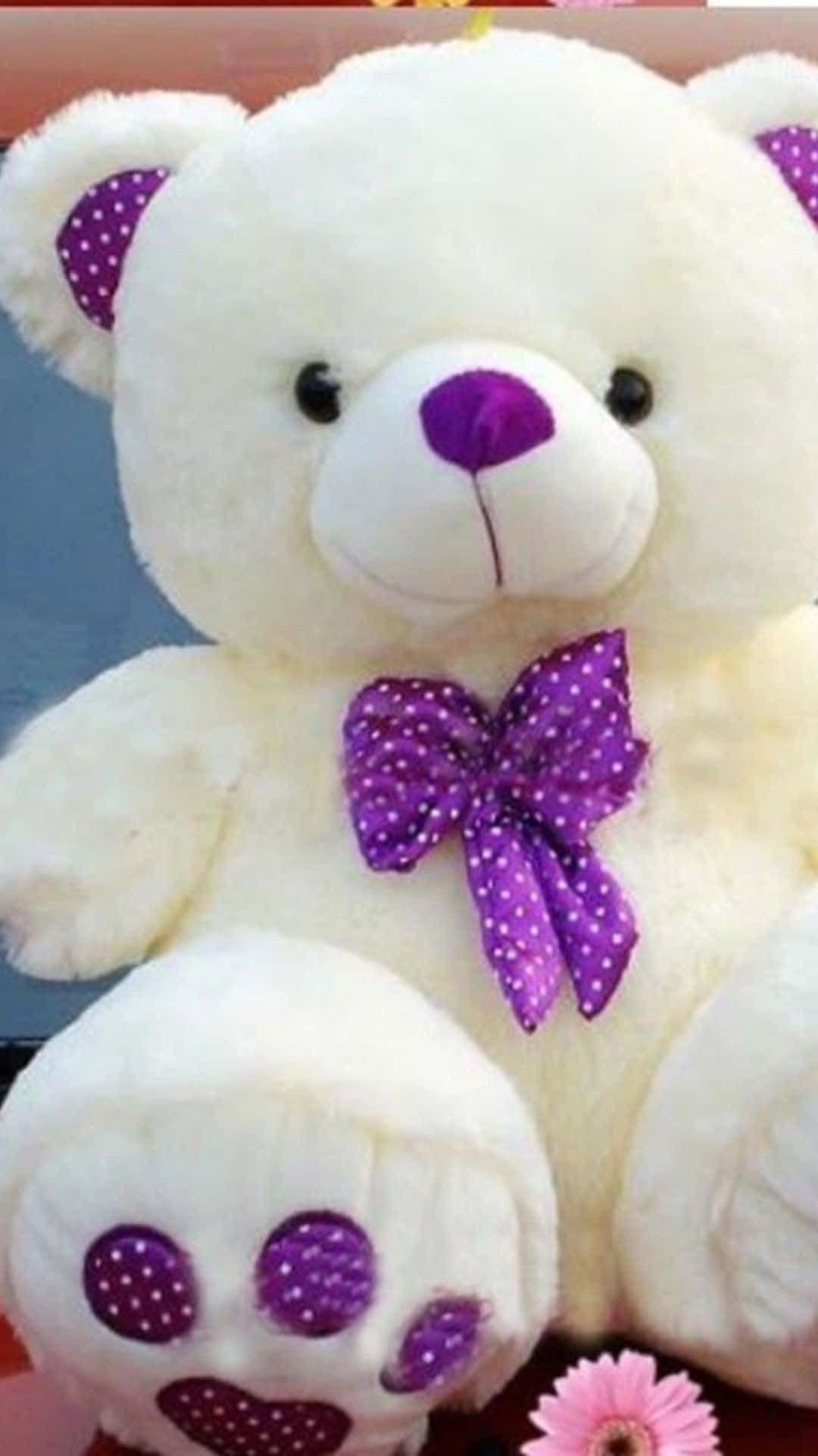 Cute Phone 桌布 壁紙 — 一隻毛茸茸的白色泰迪熊，帶有紫色圓點裝飾和相配的蝴蝶結，坐在一朵粉紅色的花旁邊。