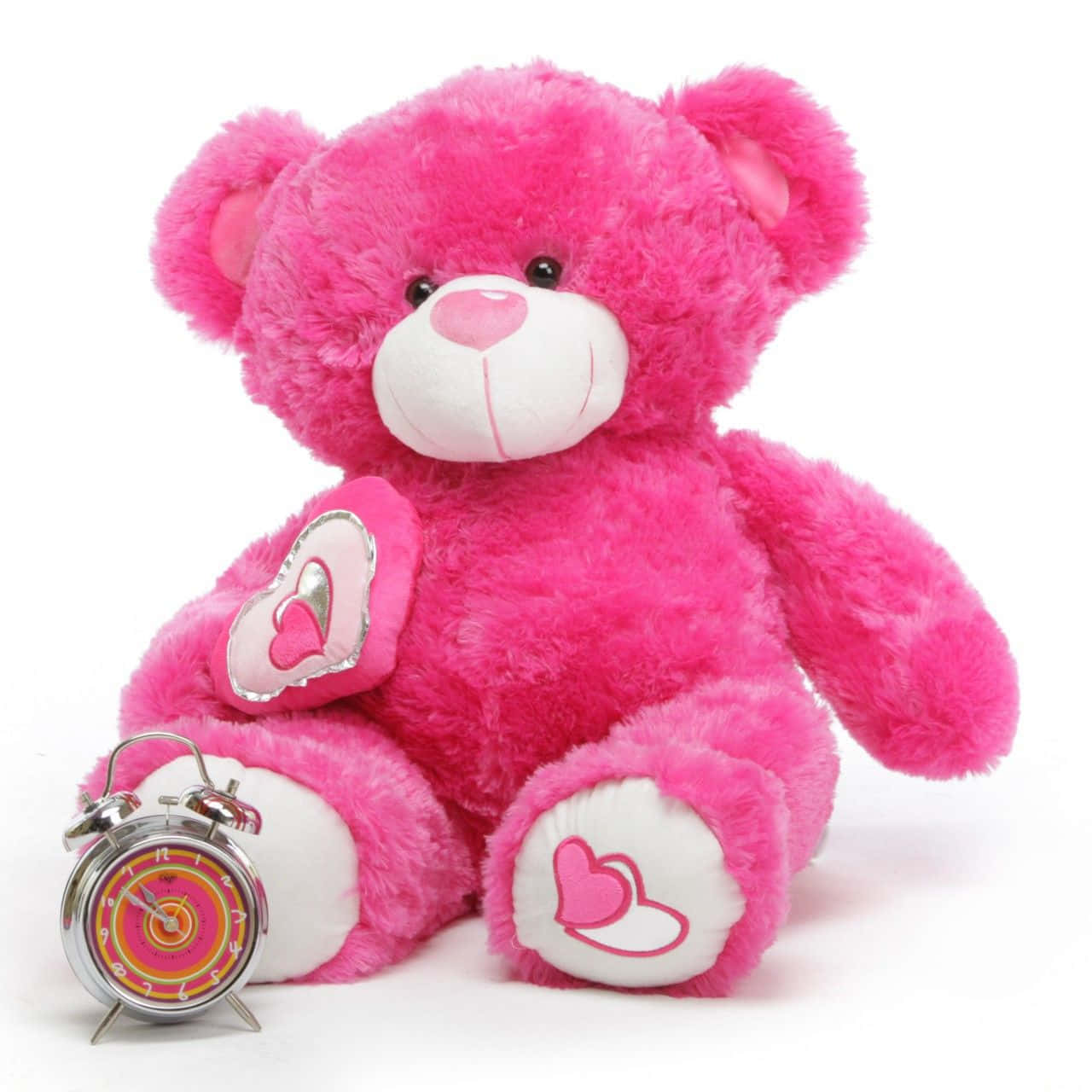 bear love 桌布 壁紙 — 一隻毛茸茸的粉紅色泰迪熊，帶有心形細節，坐在白色背景上的一個彩色鬧鐘旁邊。