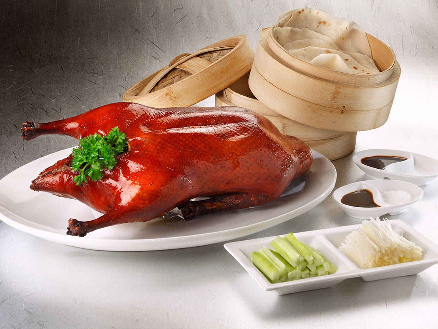 鴨子 桌布 壁紙 — 一隻油亮的烤鴨搭配新鮮香草，放在白色盤子上，旁邊有竹蒸籠和傳統配菜。