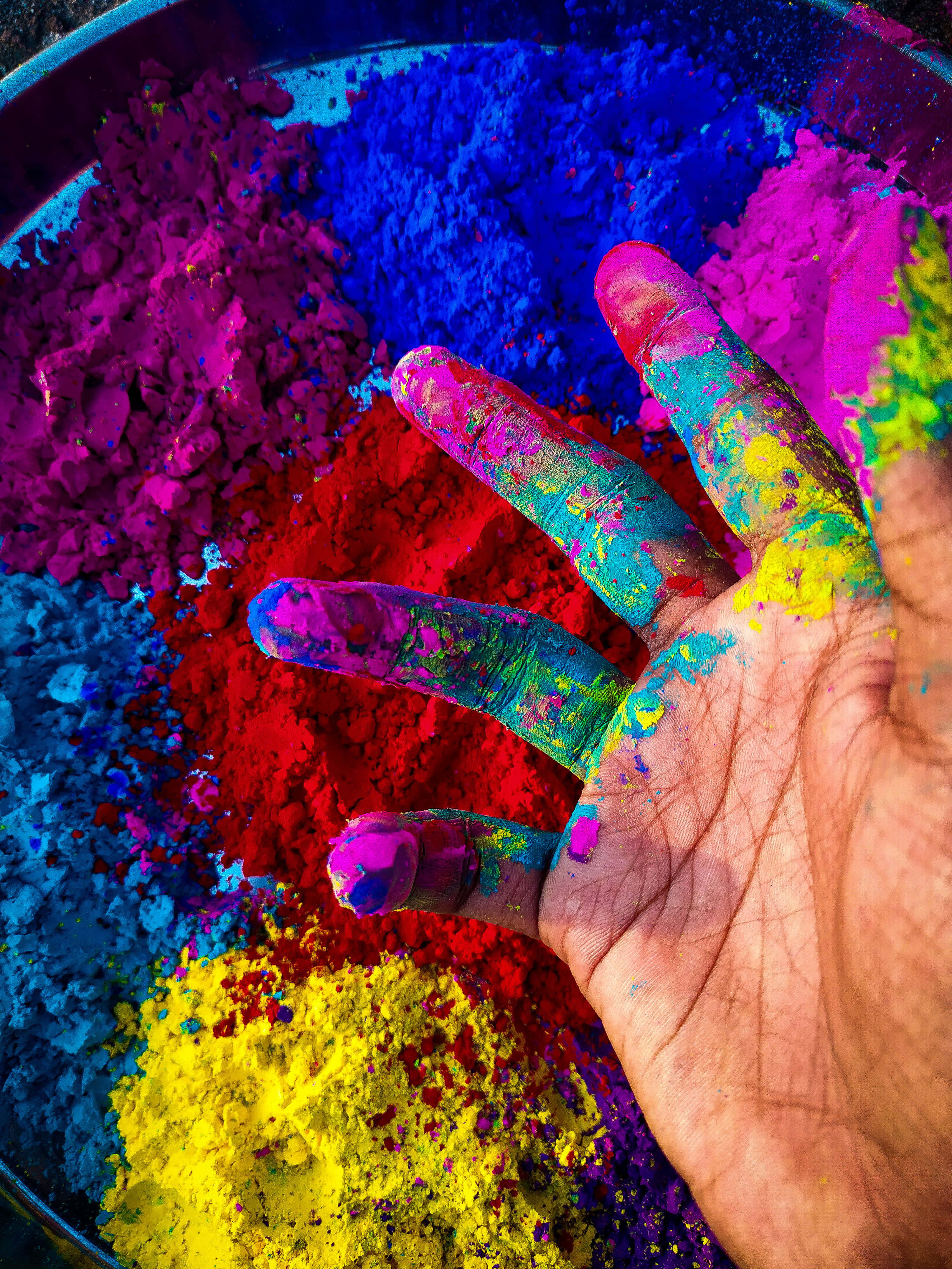 Holi 桌布 壁紙 — 一隻沾滿鮮豔彩色粉末的手，放在一碗色彩繽紛的節日塵埃上。