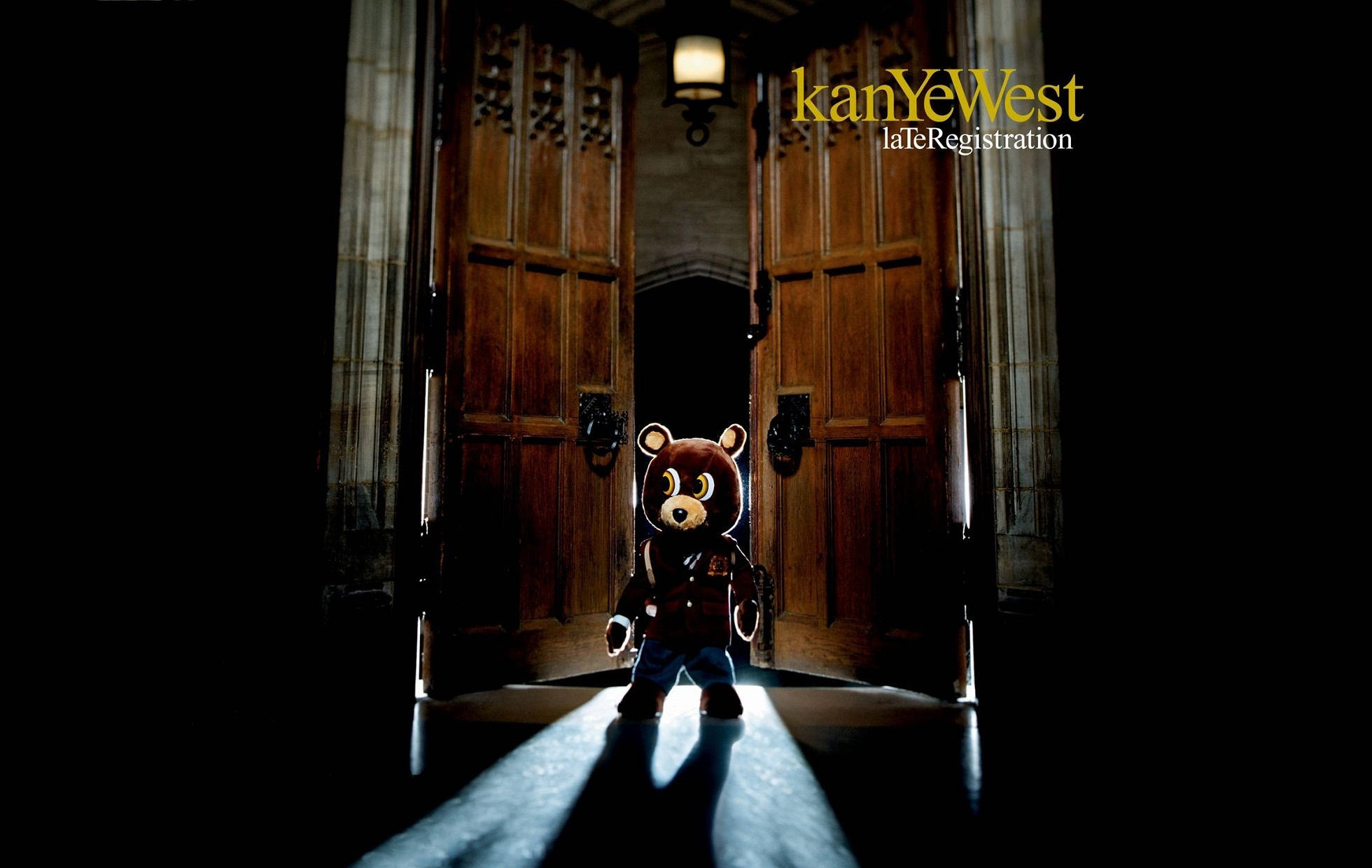 Kanye 桌布 壁紙 — 一隻泰迪熊吉祥物站在聚光燈下，位於昏暗大廳中宏偉木門的門檻處。