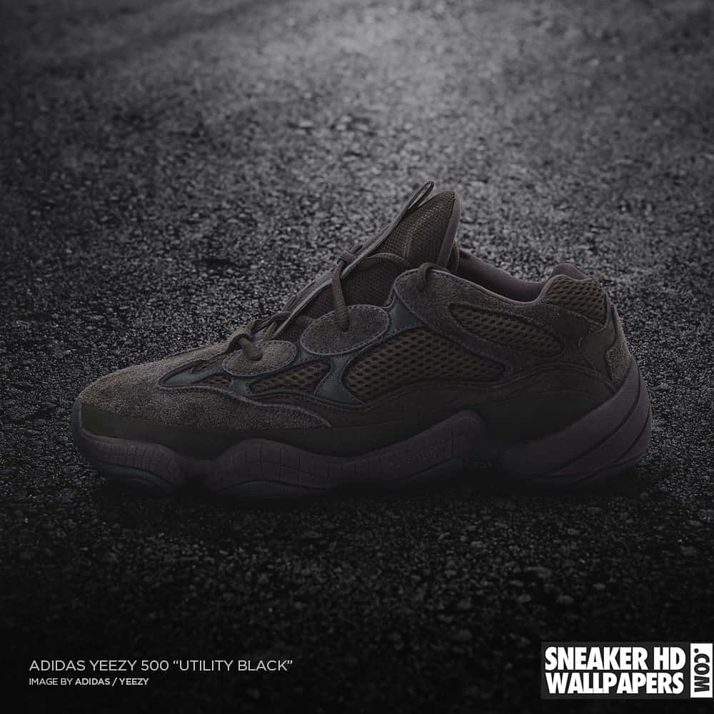 Yeezy 桌布 壁紙 — 一隻深灰色Adidas Yeezy 500 Utility Black運動鞋在戲劇性聚光燈下放在濕瀝青上。