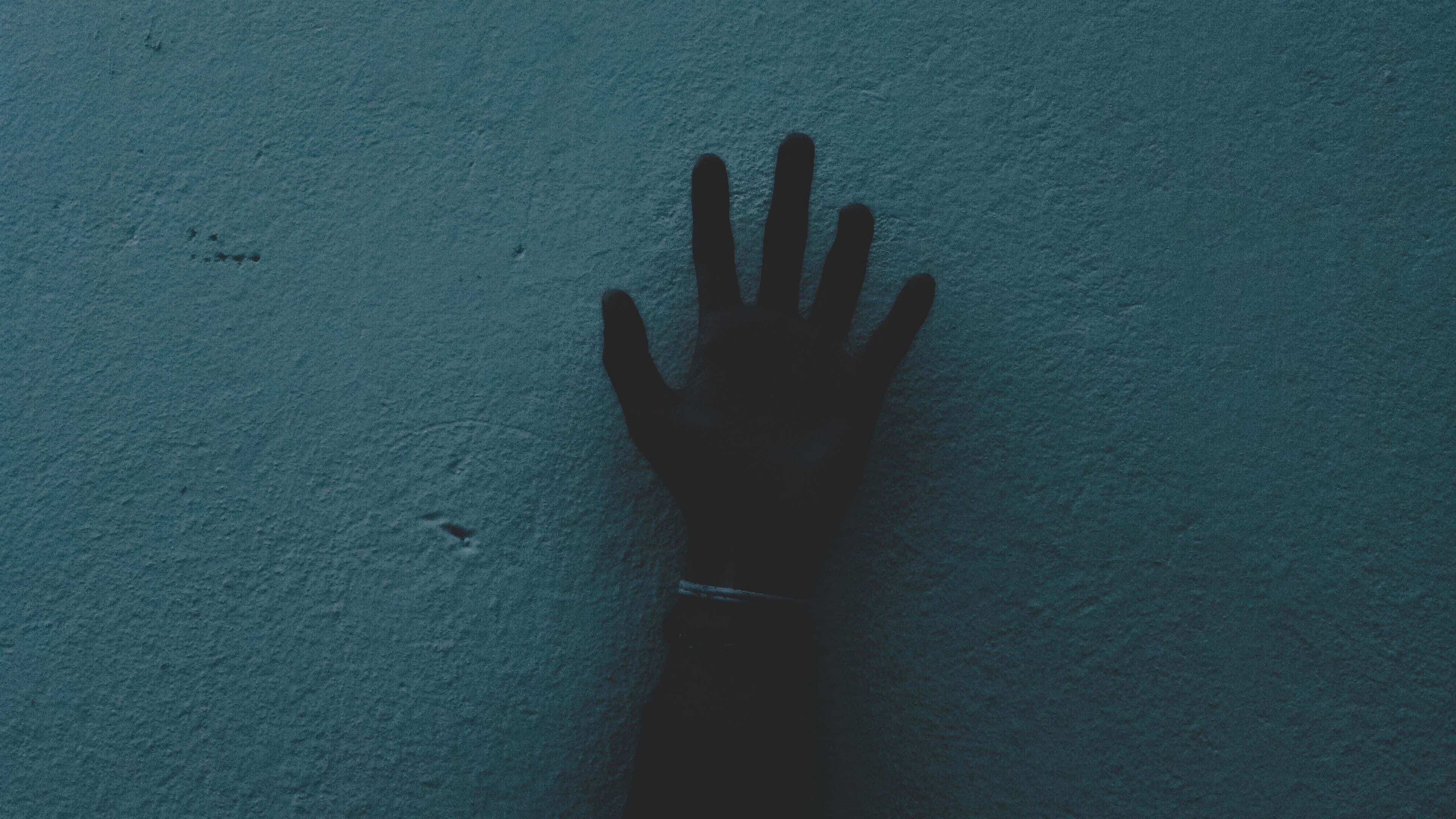 Dark Hand 桌布 壁紙 — 一隻深色的手按在帶有紋理的青綠色牆上，在昏暗燈光下投射出清晰的陰影。