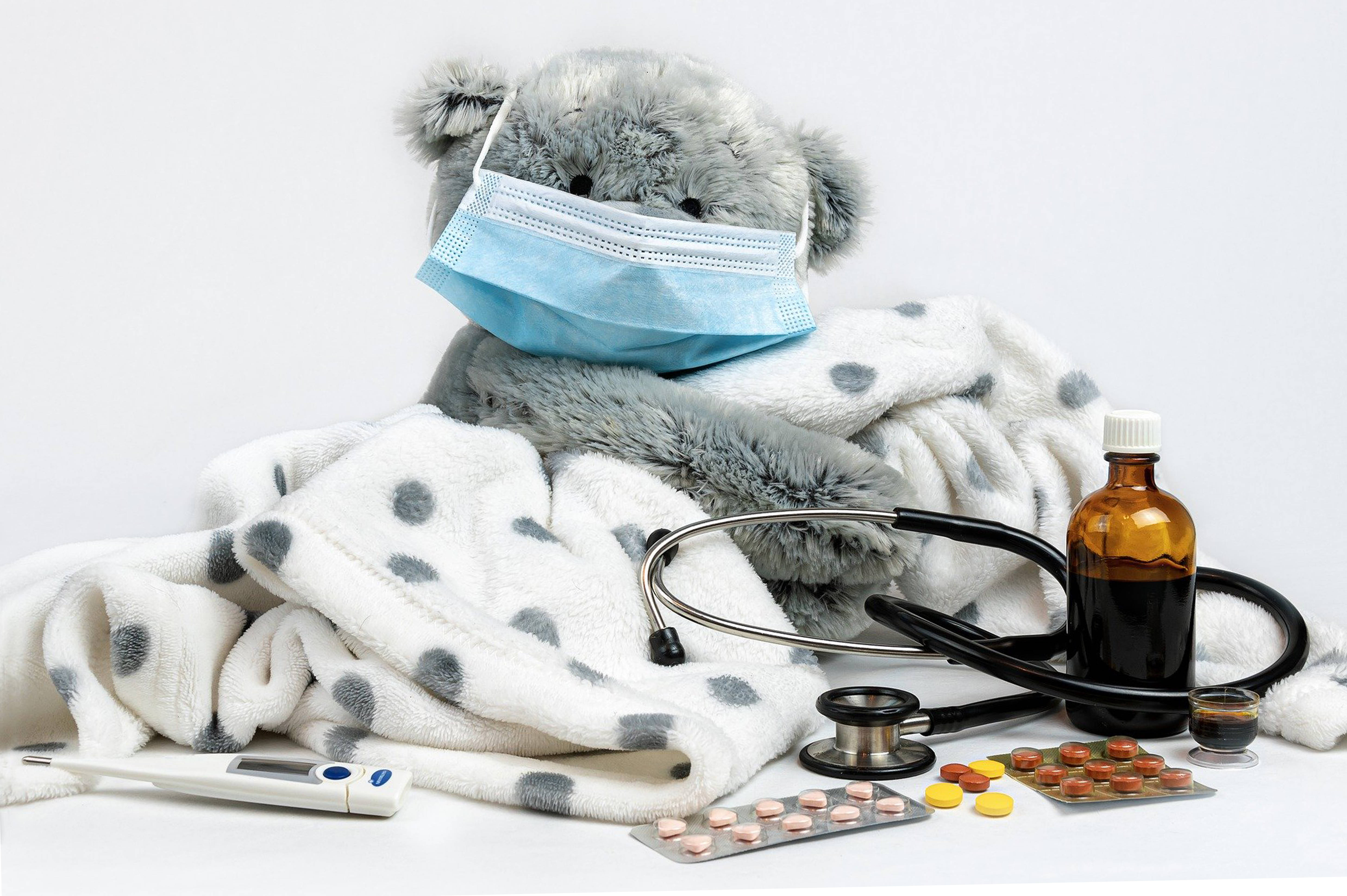 Stethoscope 桌布 壁紙 — 一隻灰色絨毛無尾熊戴著藍色外科口罩，在白色圓點毯子下休息，周圍放有醫療用品。