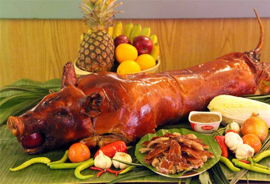 Pig 桌布 壁紙 — 一隻烤全豬，表皮焦糖化，放在香蕉葉上，周圍環繞著熱帶水果和新鮮蔬菜。
