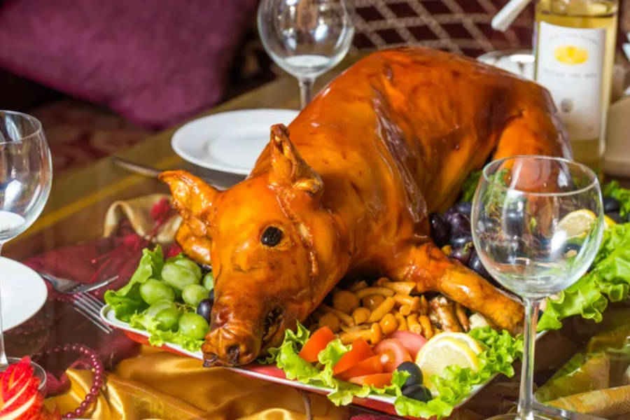 Pig 桌布 壁紙 — 一隻烤全豬，金黃酥脆的豬皮，放在盤中，周圍環繞著新鮮蔬菜和葡萄。