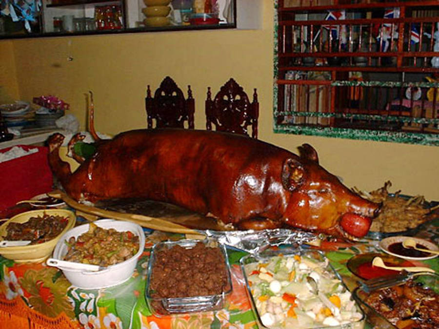 Pig 桌布 壁紙 — 一隻烤全豬，金黃酥脆的豬皮，放在木盤中央，周圍環繞著色彩繽紛的菲律賓配菜。