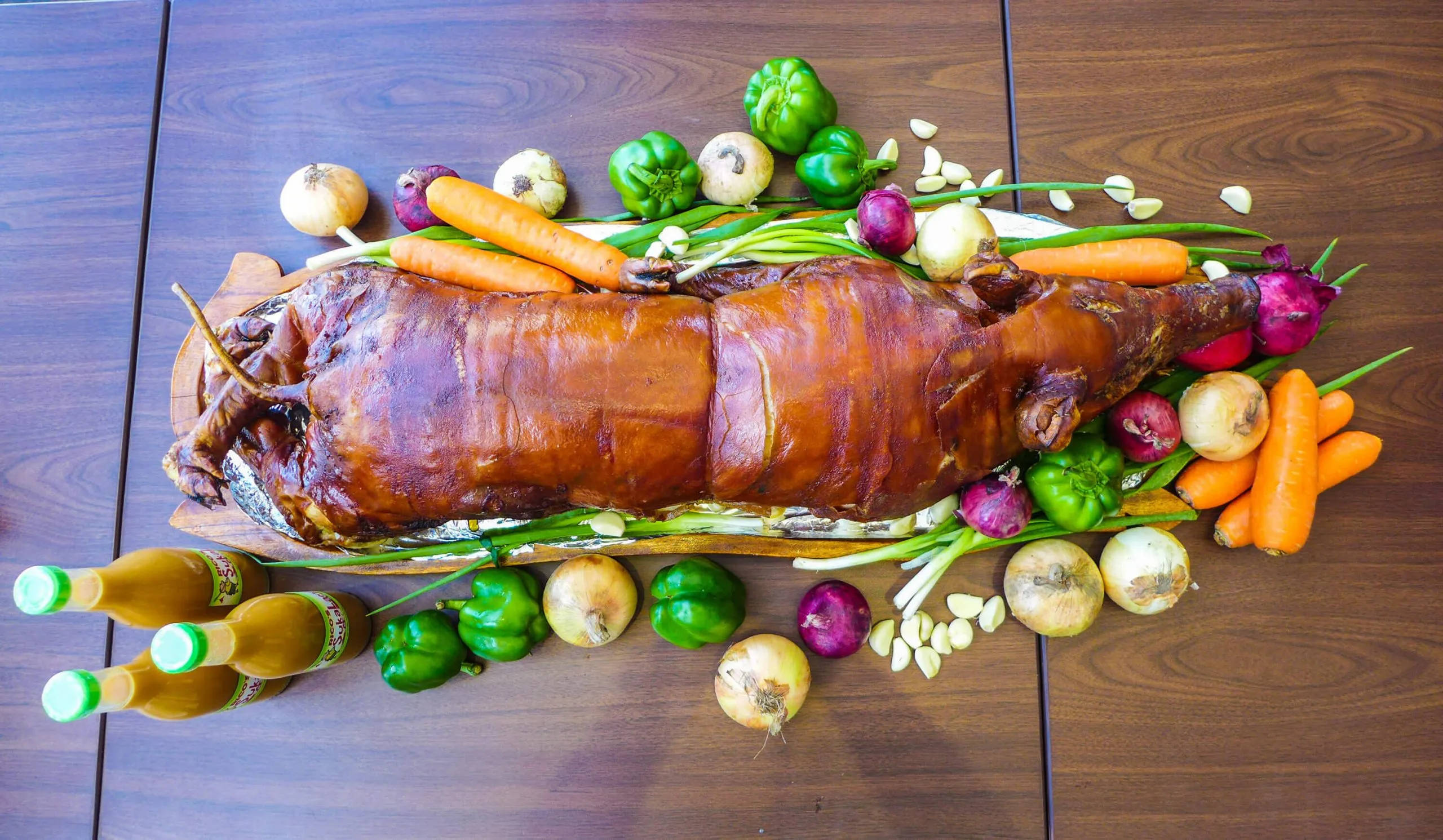 Pig 桌布 壁紙 — 一隻烤全豬，金黃酥脆的豬皮，放在木板上，周圍環繞著色彩繽紛的蔬菜和醬汁。