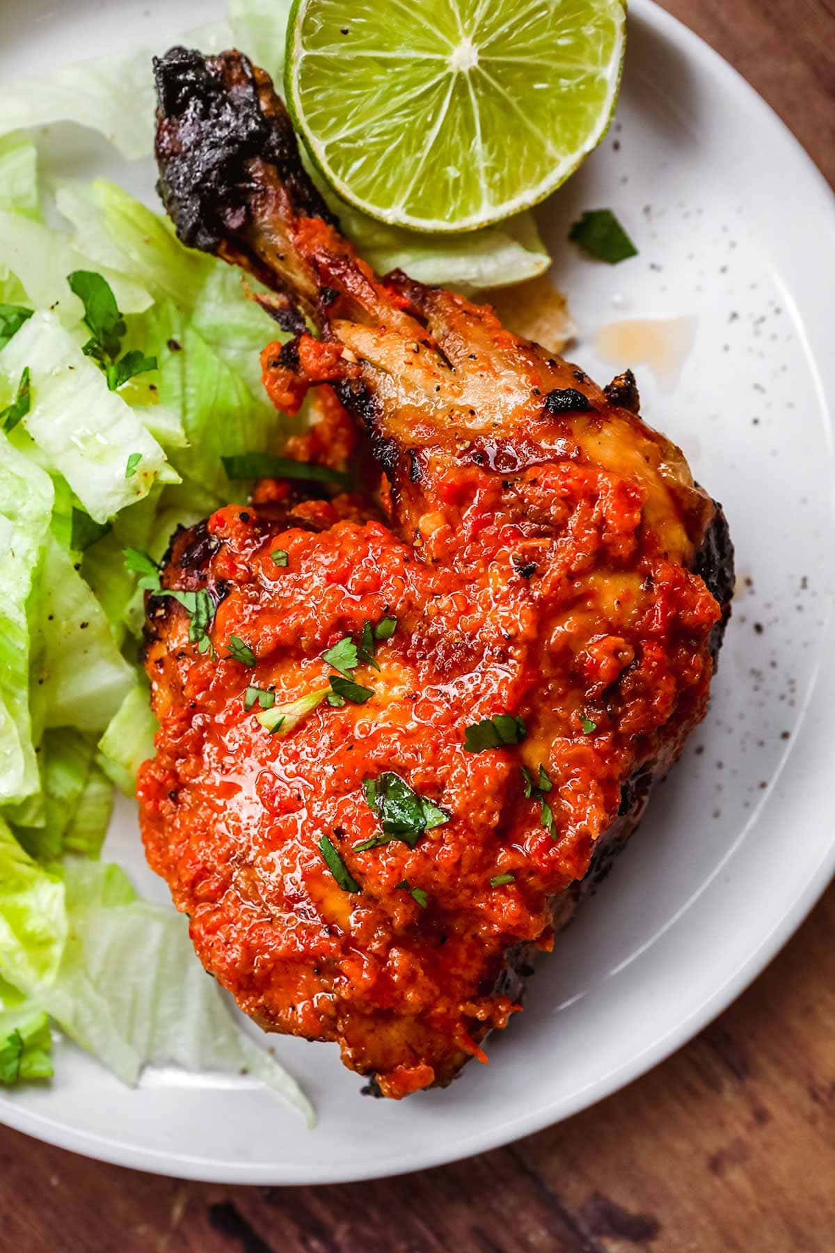 Delicious Food 桌布 壁紙 — 一隻烤雞腿浸在鮮紅色的醬汁中，旁邊放著脆生菜和萊姆角，放在一個有斑點的盤子上。
