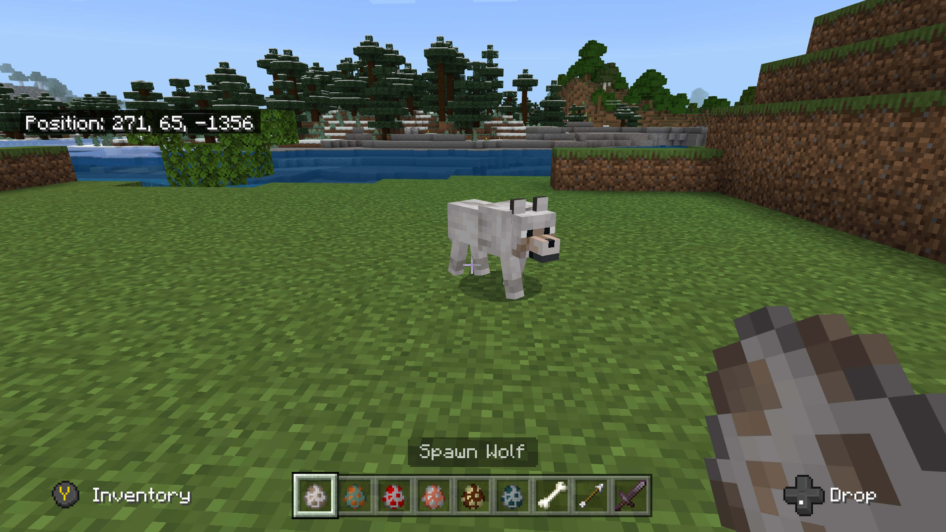 Minecraft Wolf 桌布 壁紙 — 一隻白狼在一個有樹木和山丘的方塊Minecraft世界中，站在水邊的草地上，天空晴朗。