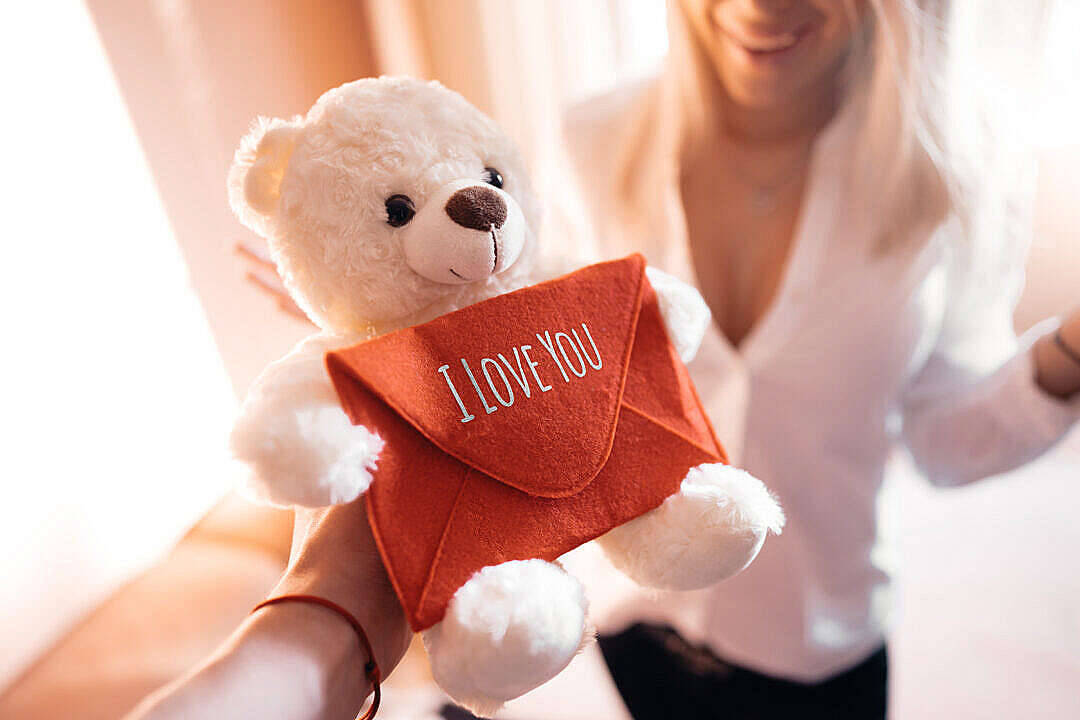 可愛泰迪熊 桌布 壁紙 — 一隻白色泰迪熊拿著一個寫有I LOVE YOU的紅色信封，由一個微笑的人呈現在柔和溫暖的光線中。