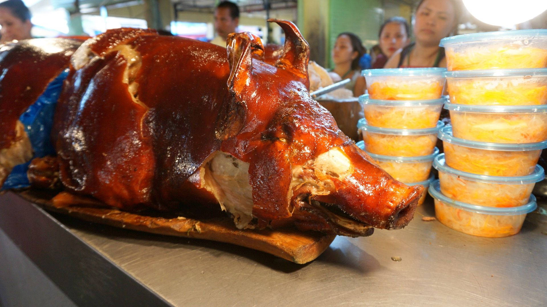 Pig 桌布 壁紙 — 一隻皮脆金黃的烤全豬放在木板上，旁邊有疊起的橙色配菜容器。