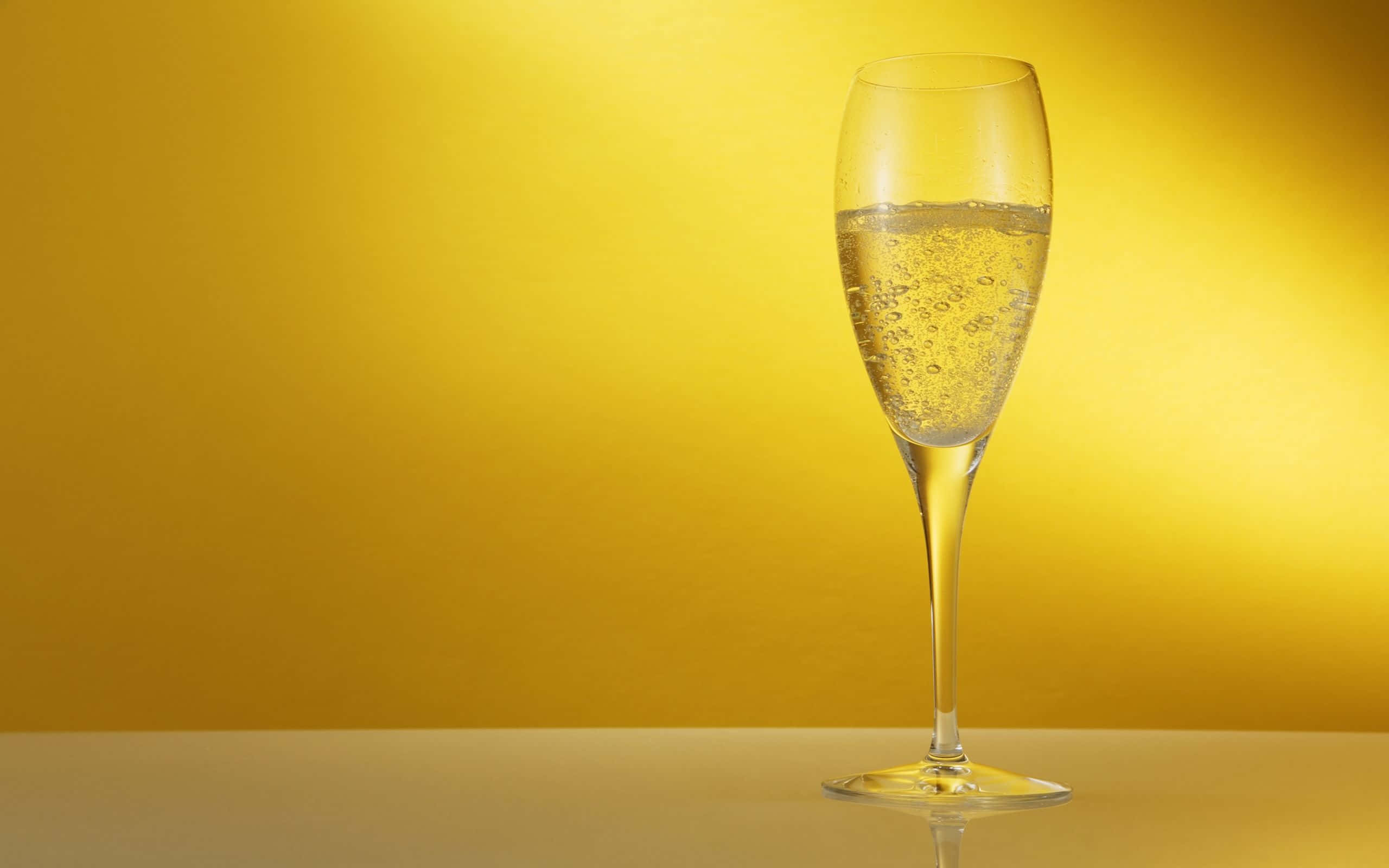 White Wine 桌布 壁紙 — 一隻盛滿閃爍氣泡酒的香檳笛形杯，優雅地矗立在耀眼的金黃色漸變背景前。