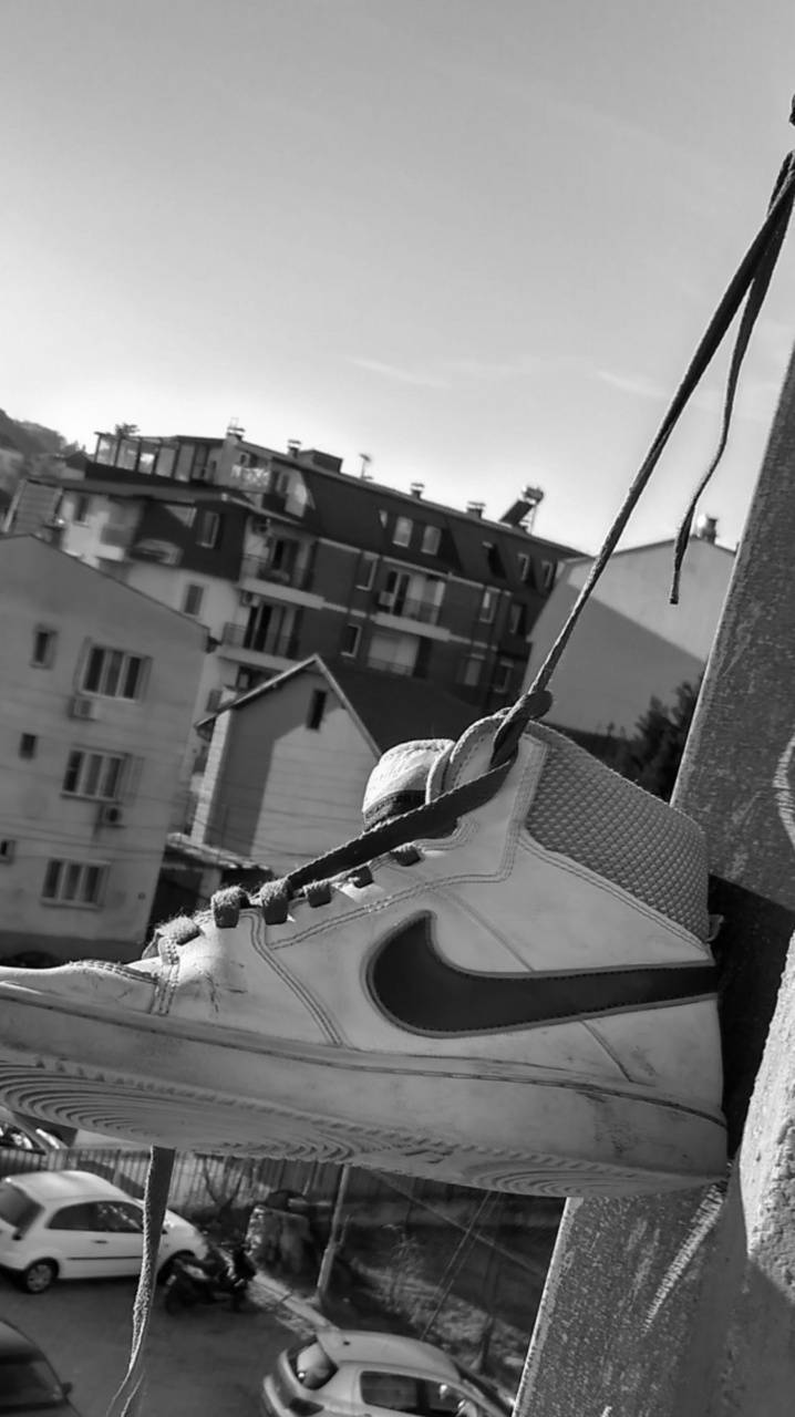 桌布 壁紙 — 一隻破舊的Nike運動鞋用鞋帶掛在混凝土邊緣上，背景是城市公寓大樓。