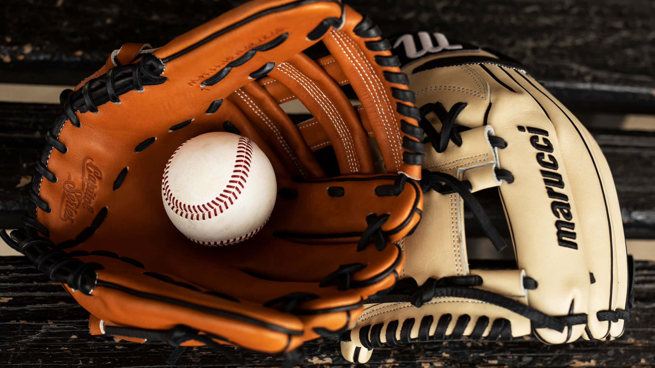 Baseball Gloves 桌布 壁紙 — 一隻磨損的棕色棒球手套在深色木質表面上托著一個帶紅色縫線的白色棒球。