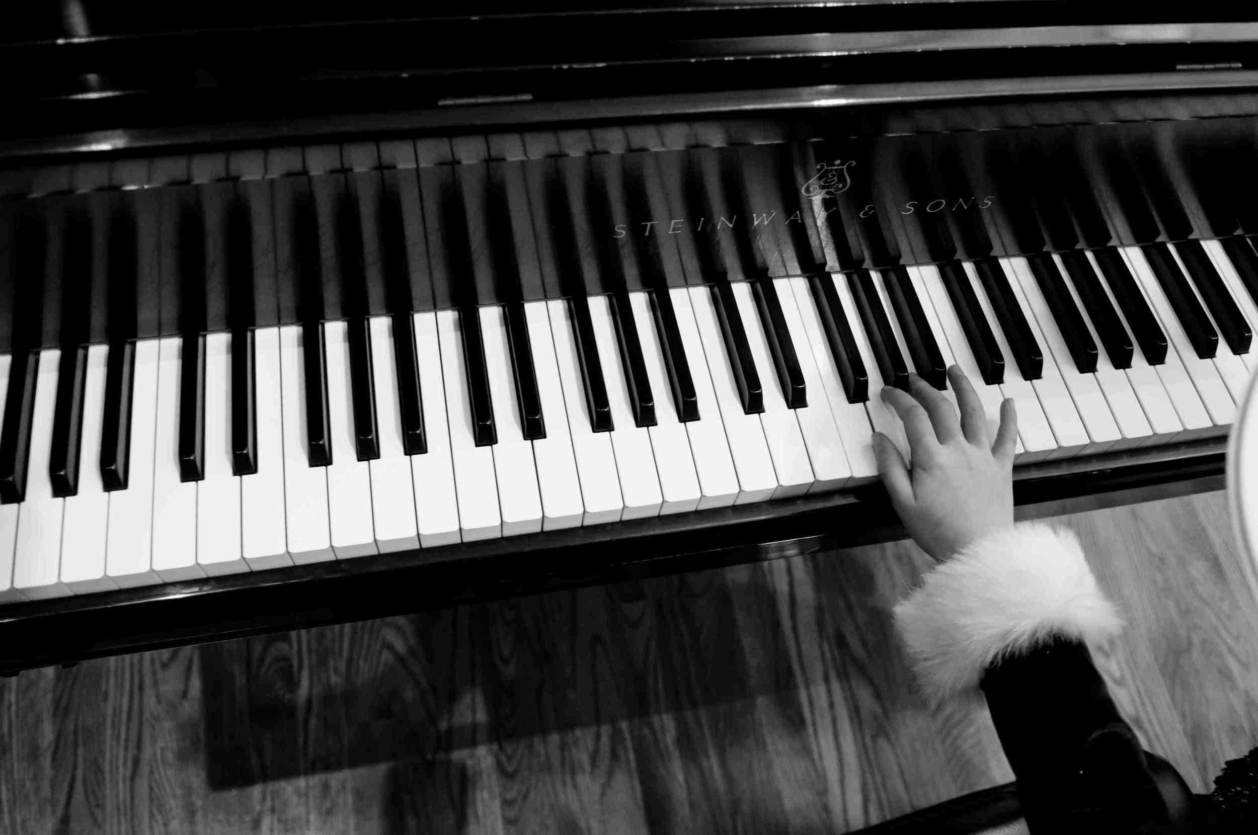 Black And White Piano 桌布 壁紙 — 一隻穿著毛茸茸袖子的孩子的手輕輕放在黑白單色史坦威鋼琴的琴鍵上。