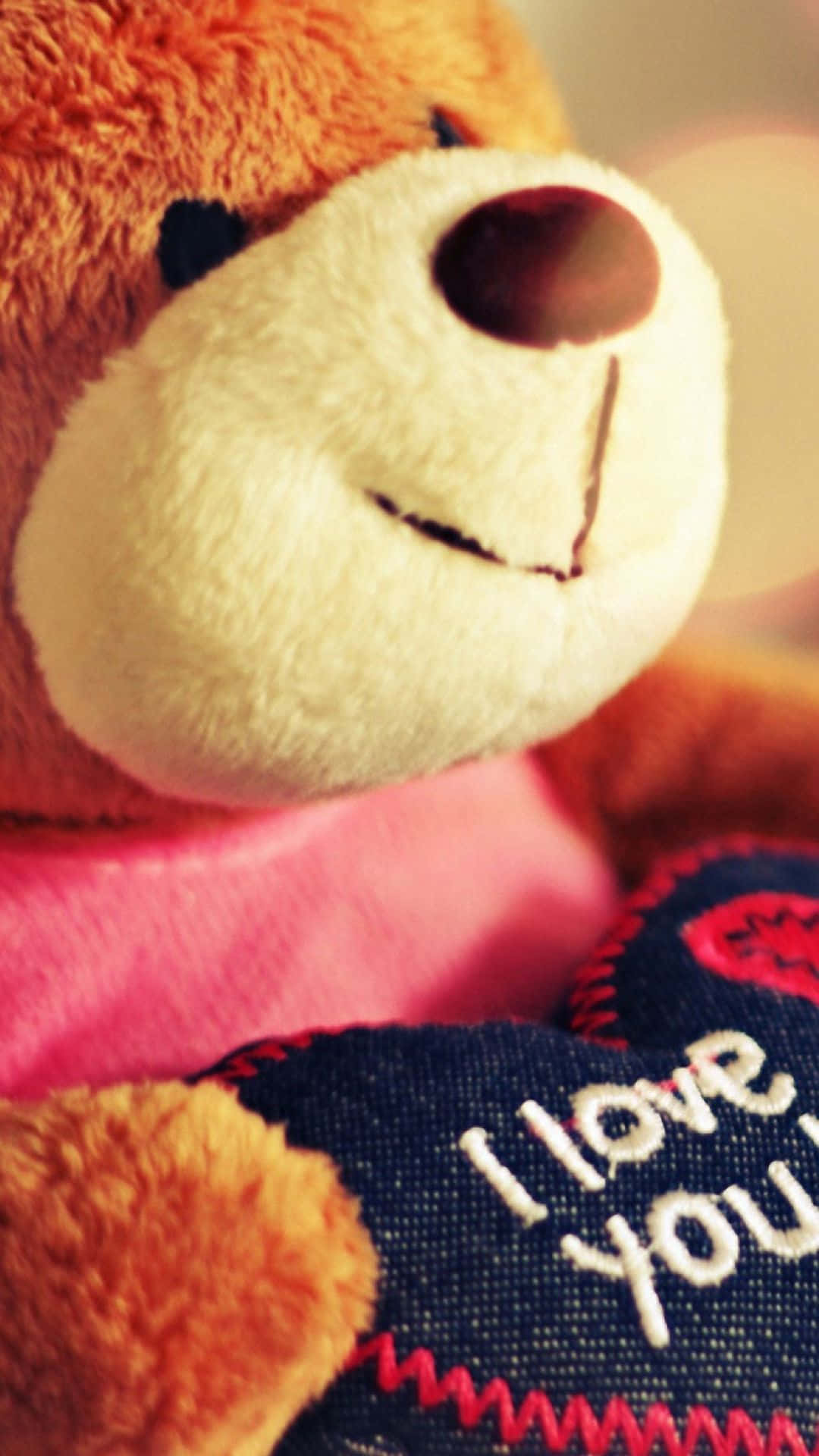 Cute Phone 桌布 壁紙 — 一隻穿著粉紅色襯衫的棕色泰迪熊近距離特寫，手持一個寫有 i love you 的牛仔布心形。