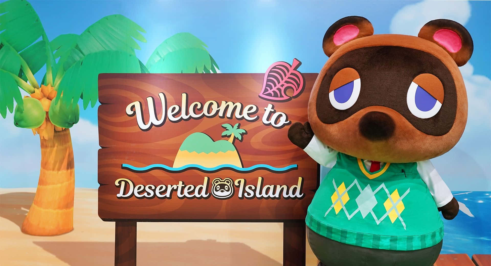 Welcome Gaming 桌布 壁紙 — 一隻穿著綠色毛衣的快樂熊角色在寫著「Welcome to Deserted Island」的木牌旁揮手，背景是明亮的藍天和棕櫚樹。