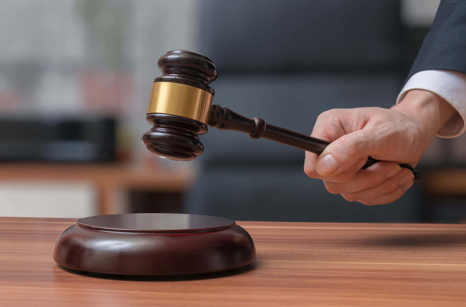 Law 桌布 壁紙 — 一隻穿著西裝的手，握著一個帶有金色環的木槌，懸停在拋光辦公桌上配套的共鳴塊上方。