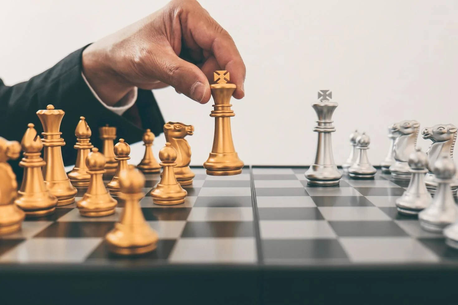 西洋棋 桌布 壁紙 — 一隻穿著西裝的手在棋盤上移動金色國王棋子，面對銀色棋子。