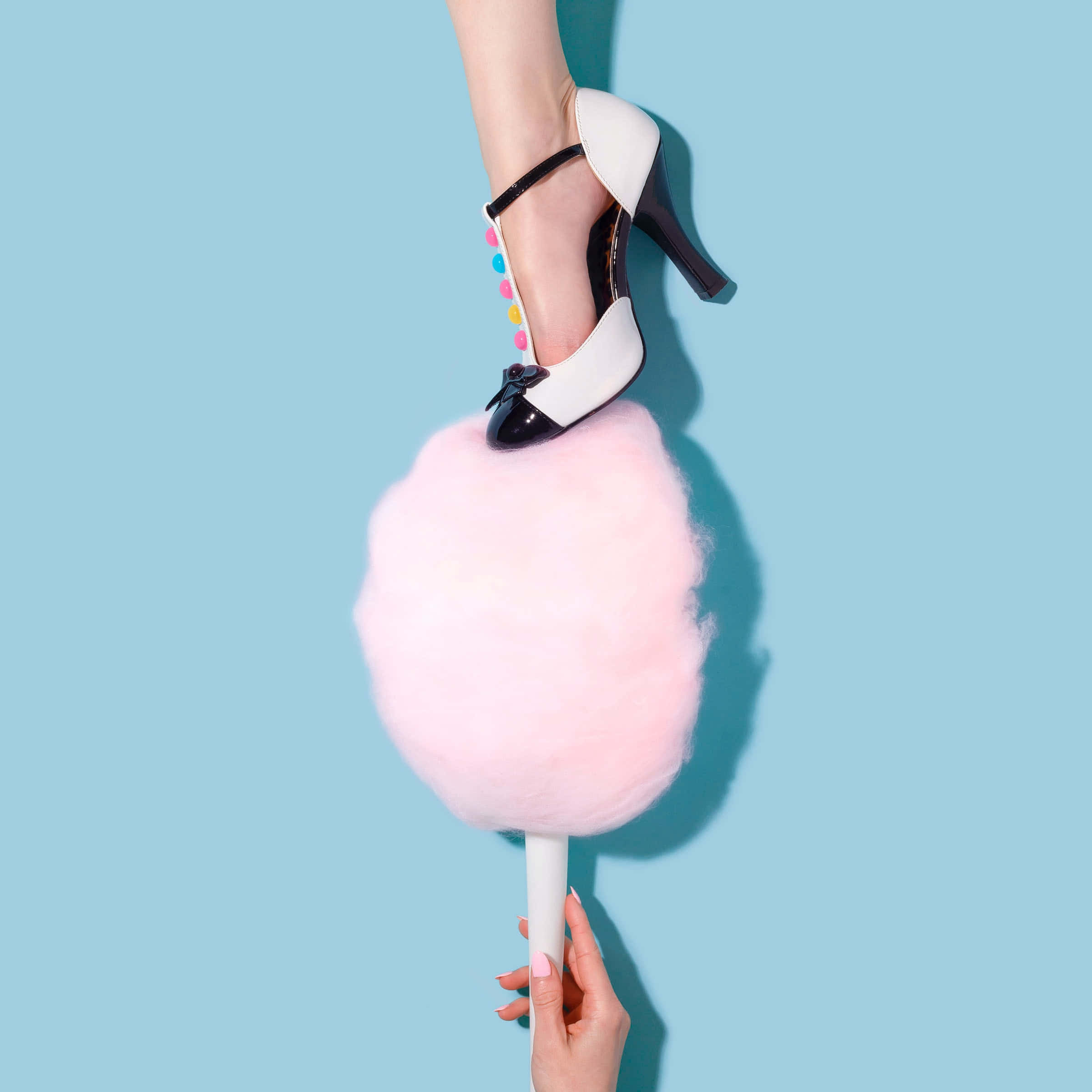 Cotton Candy 桌布 壁紙 — 一隻穿著黑白高跟鞋的腳，棲息在一根棍子上的巨大粉紅色棉花糖上，背景是純藍色。