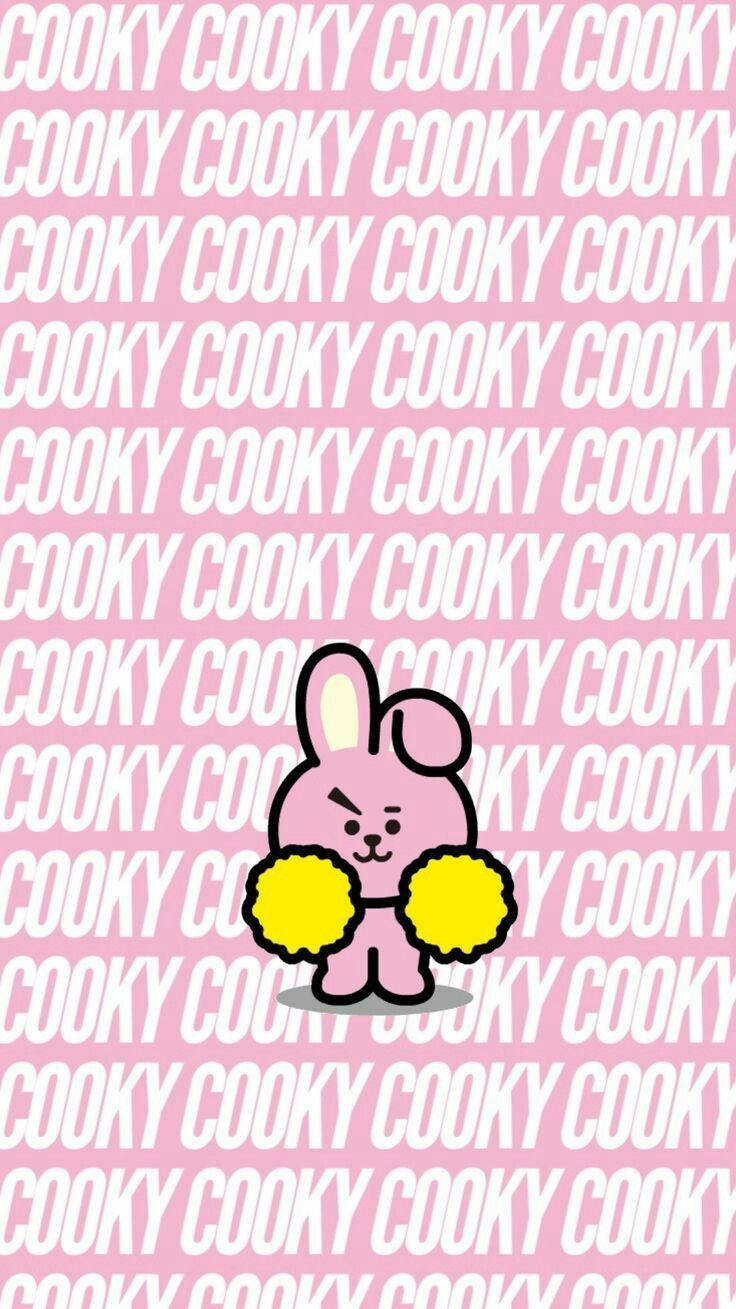 Cooky Bt21 桌布 壁紙 — 一隻粉紅色卡通兔子拿著黃色絨球，站在重複的粉紅和白色 'COOKY' 文字背景前。