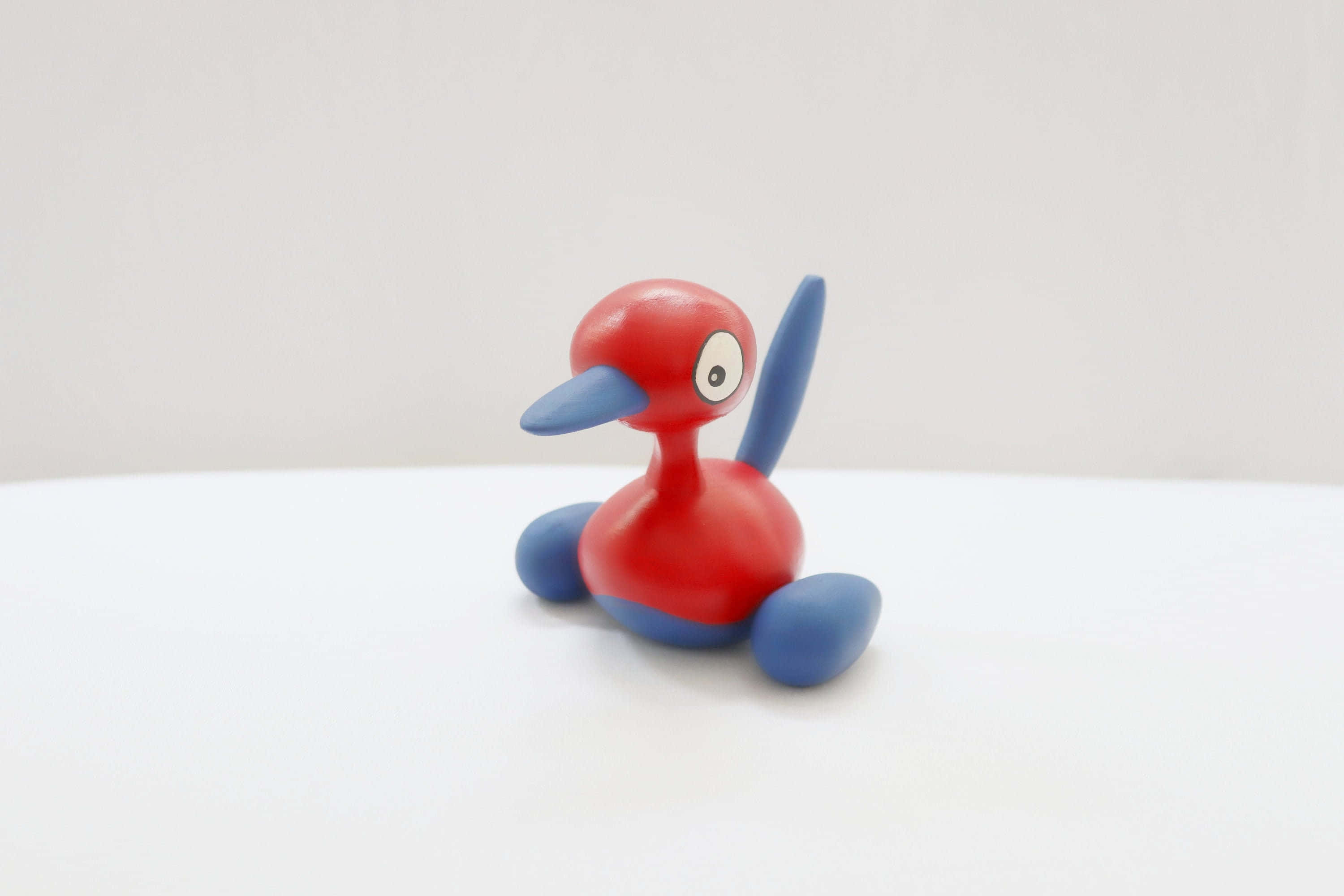 Porygon2 桌布 壁紙 — 一隻紅色和藍色的卡通鴨玩具，有大眼睛，坐在白色表面上，背景是純白色。