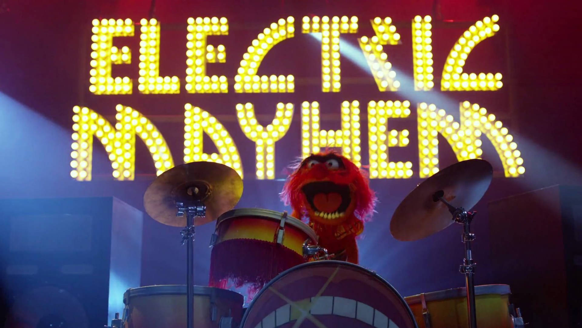 muppets 桌布 壁紙 — 一隻紅色毛茸茸的Muppet鼓手在昏暗的舞台上，在發光的「ELECTRIC MAYHEM」標誌下打著一套色彩繽紛的鼓。