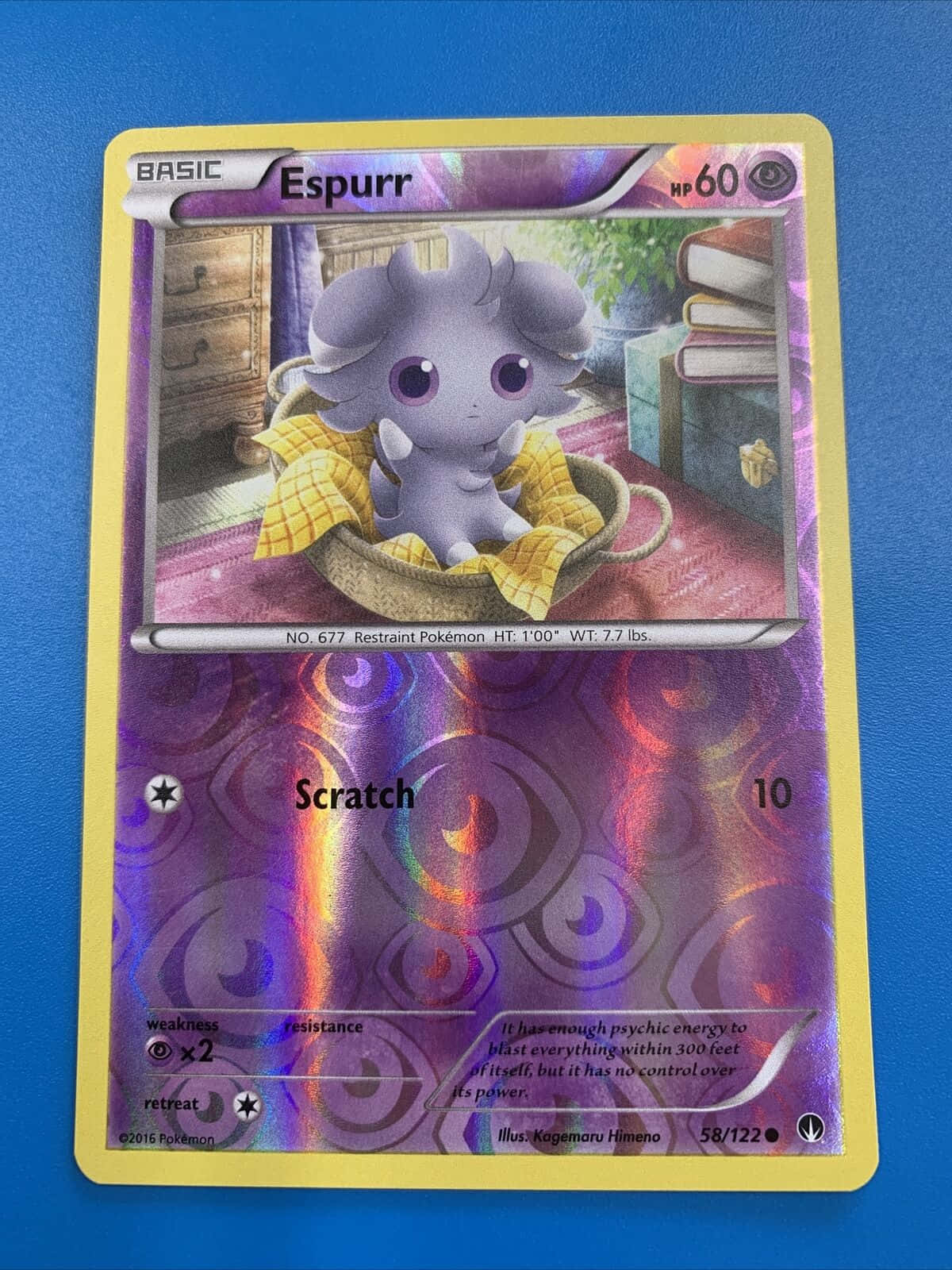 espurr 桌布 壁紙 — 一隻紫色的超能妙喵坐在一個鋪著黃色布的編織籃子裡，籃子放在粉紅色的地毯上，周圍是書本和傢俱，在一個舒適的房間裡。