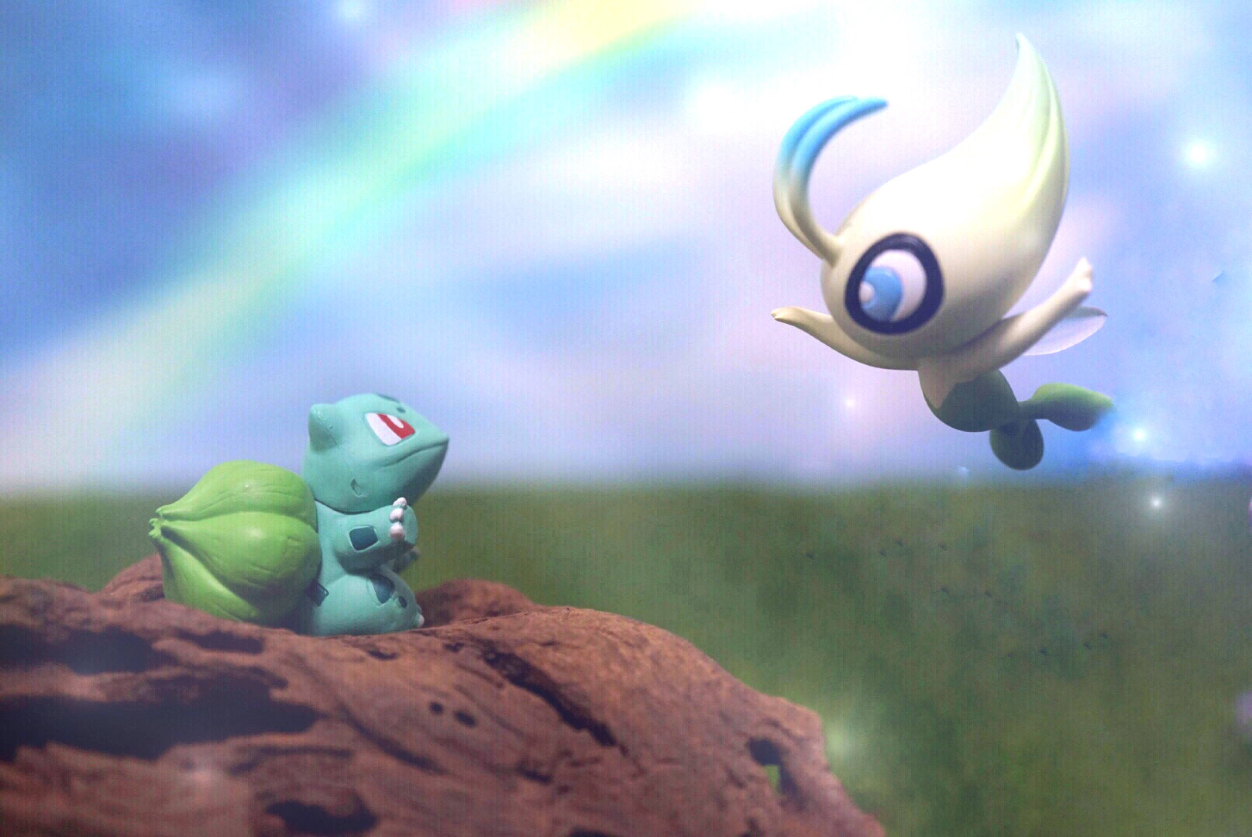 Bulbasaur 桌布 壁紙 — 一隻綠色的 Bulbasaur 坐在岩石上，仰望一隻白色的 Lumiose 飛行生物，背景是彩虹天空。