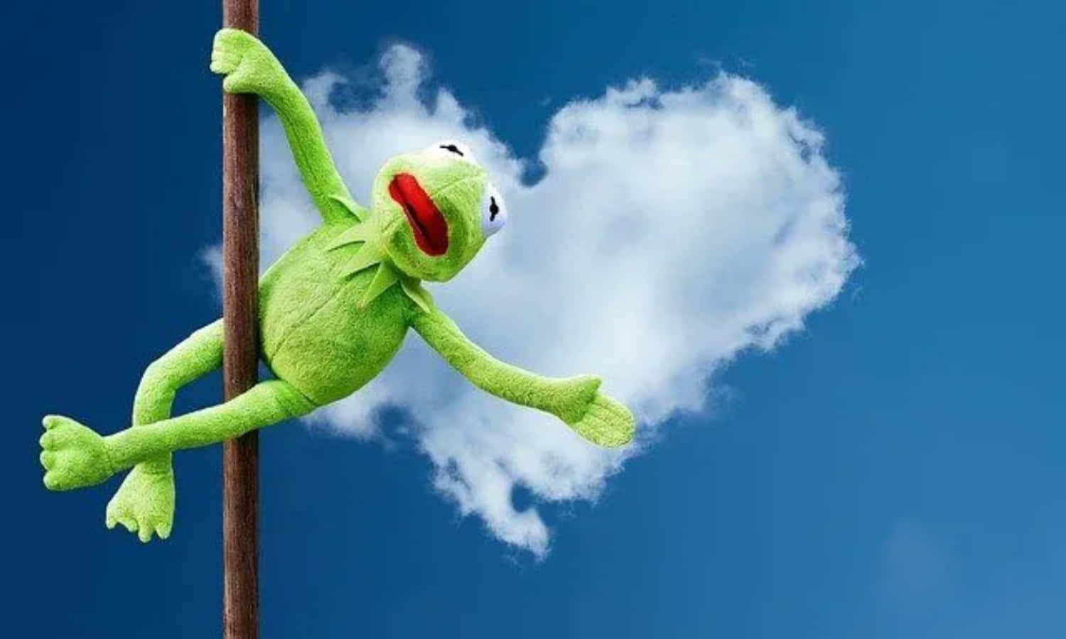 雲朵 桌布 壁紙 — 一隻綠色的Kermit the Frog絨毛玩具掛在柱子上，背景是藍天，旁邊有心形雲。