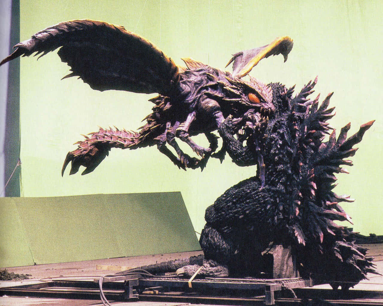 Godzilla Vs Megaguirus 桌布 壁紙 — 一隻背脊有刺、有翅膀的哥斯拉式怪獸在綠幕場景中攻擊一隻較小的龍形怪獸。