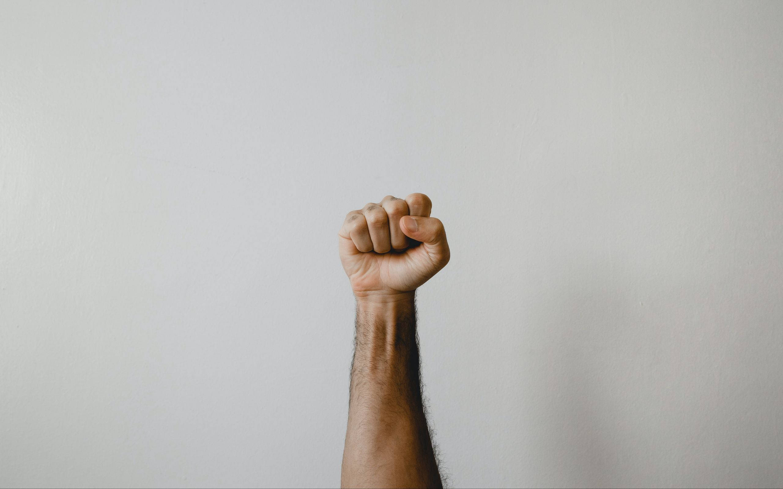 fist pump 桌布 壁紙 — 一隻舉起的拳頭對著純白牆壁，象徵力量與團結。