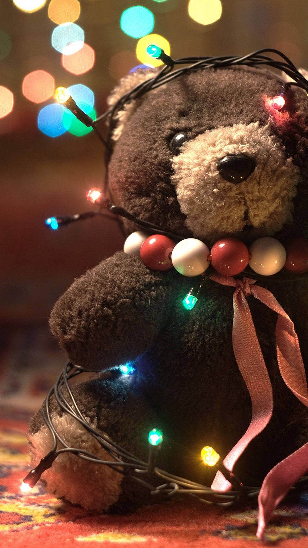 Teddy Bear 桌布 壁紙 — 一隻舒適的棕色泰迪熊，裝飾著彩色燈串和珠鏈，在散景背景下溫暖地坐著。