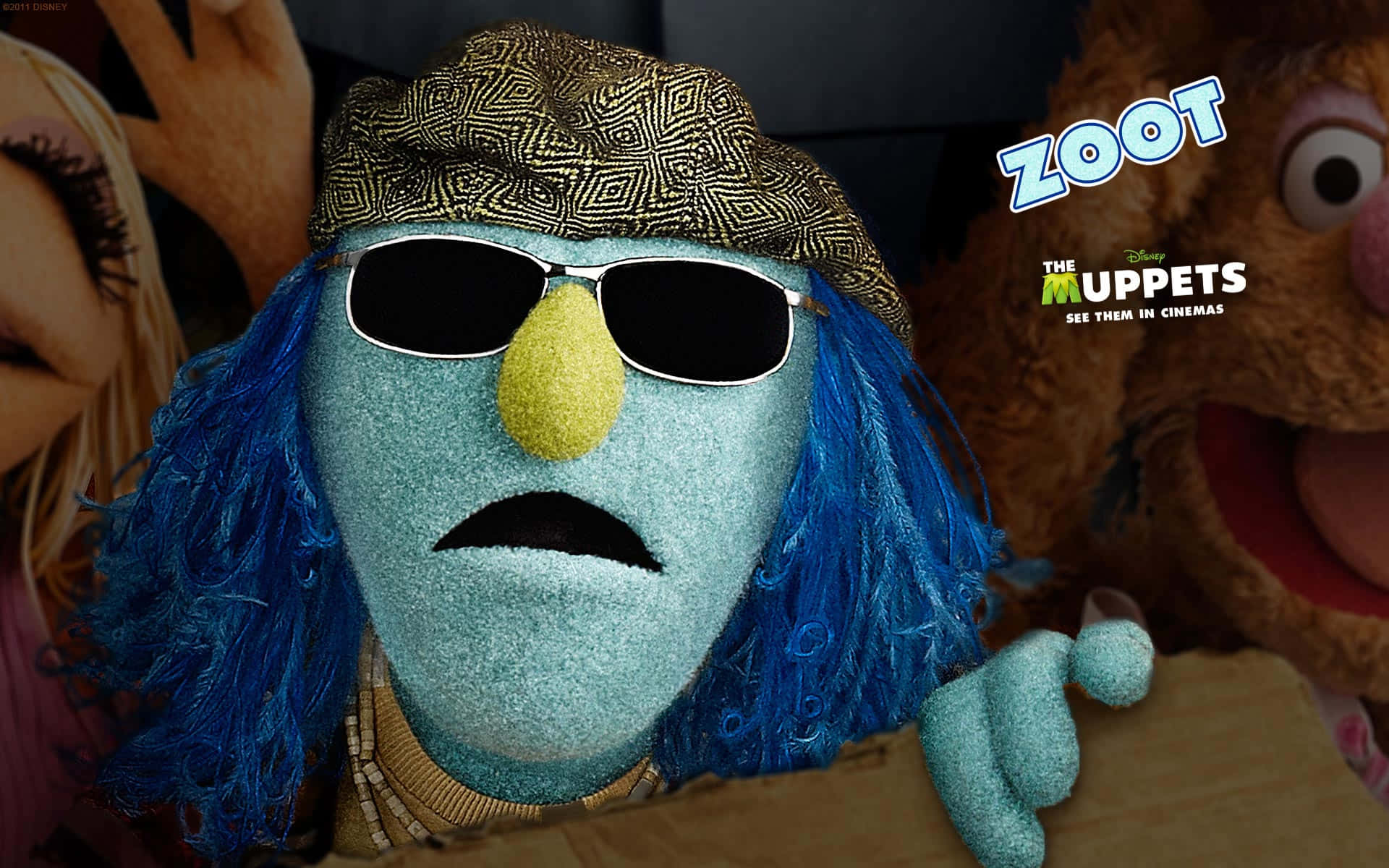 Animal Muppet 桌布 壁紙 — 一隻藍色Muppet戴着太陽眼鏡和圖案帽子，在其他Muppet圍繞的宣傳場景中顯得很酷。