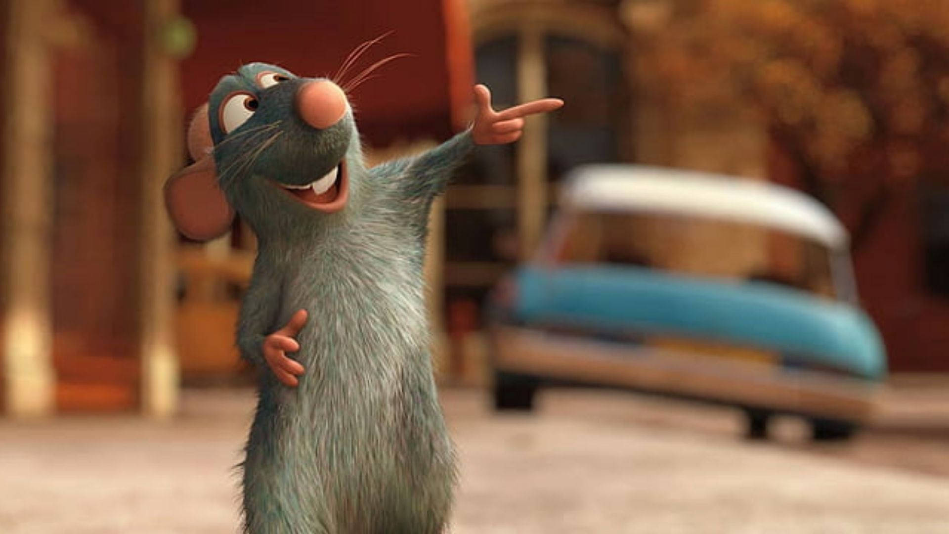 Ratatouille 桌布 壁紙 — 一隻藍色毛髮、粉紅色鼻子的開心動畫老鼠在充滿活力的街景中興奮地指著。